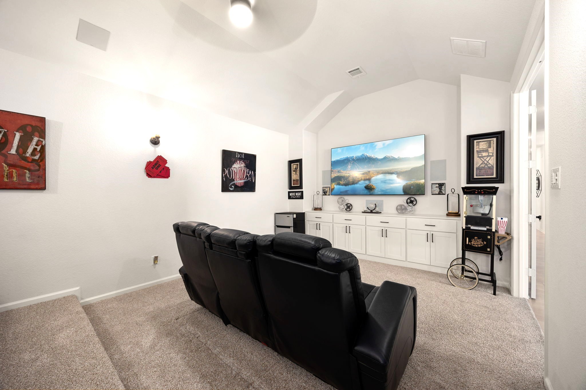 A fully equipped home theater features custom cabinetry and drawers, built-in in-wall speakers, a popcorn machine, and a mini fridge, creating a private cinema experience designed for effortless entertaining and unforgettable movie nights.