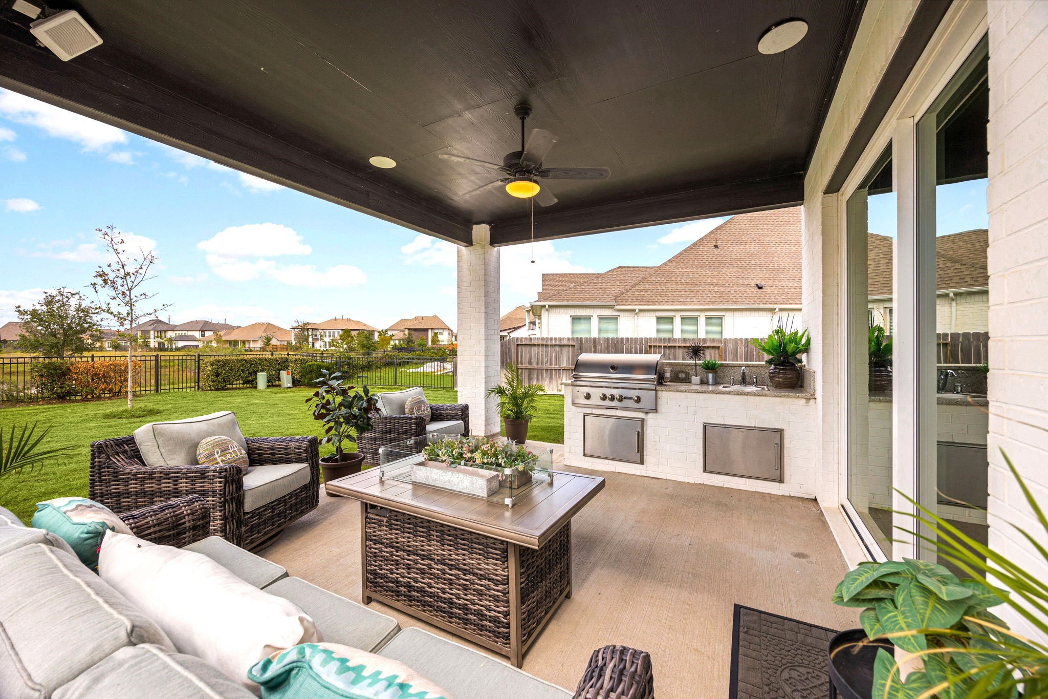 An upgraded covered outdoor living space features a built-in grill, sink, ceiling fan, and inviting fire pit, creating the perfect setting for year-round entertaining, relaxed evenings, and elevated outdoor living.