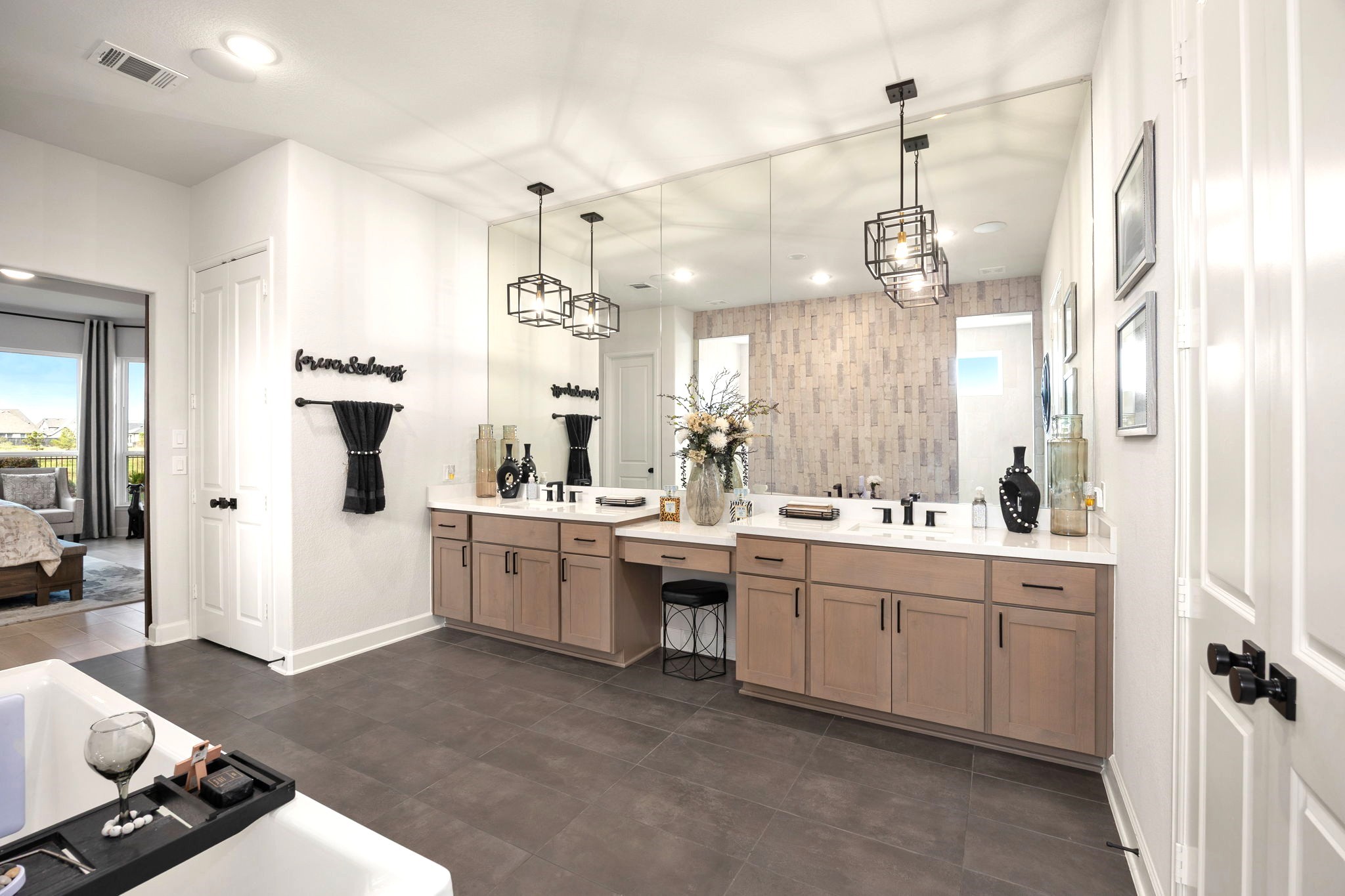 A luxurious primary bathroom features dual vanities with upgraded cabinet hardware, elegant pendant lighting, and an expansive wall-to-wall mirror, creating a sophisticated, spa-inspired retreat with elevated finishes and timeless style.