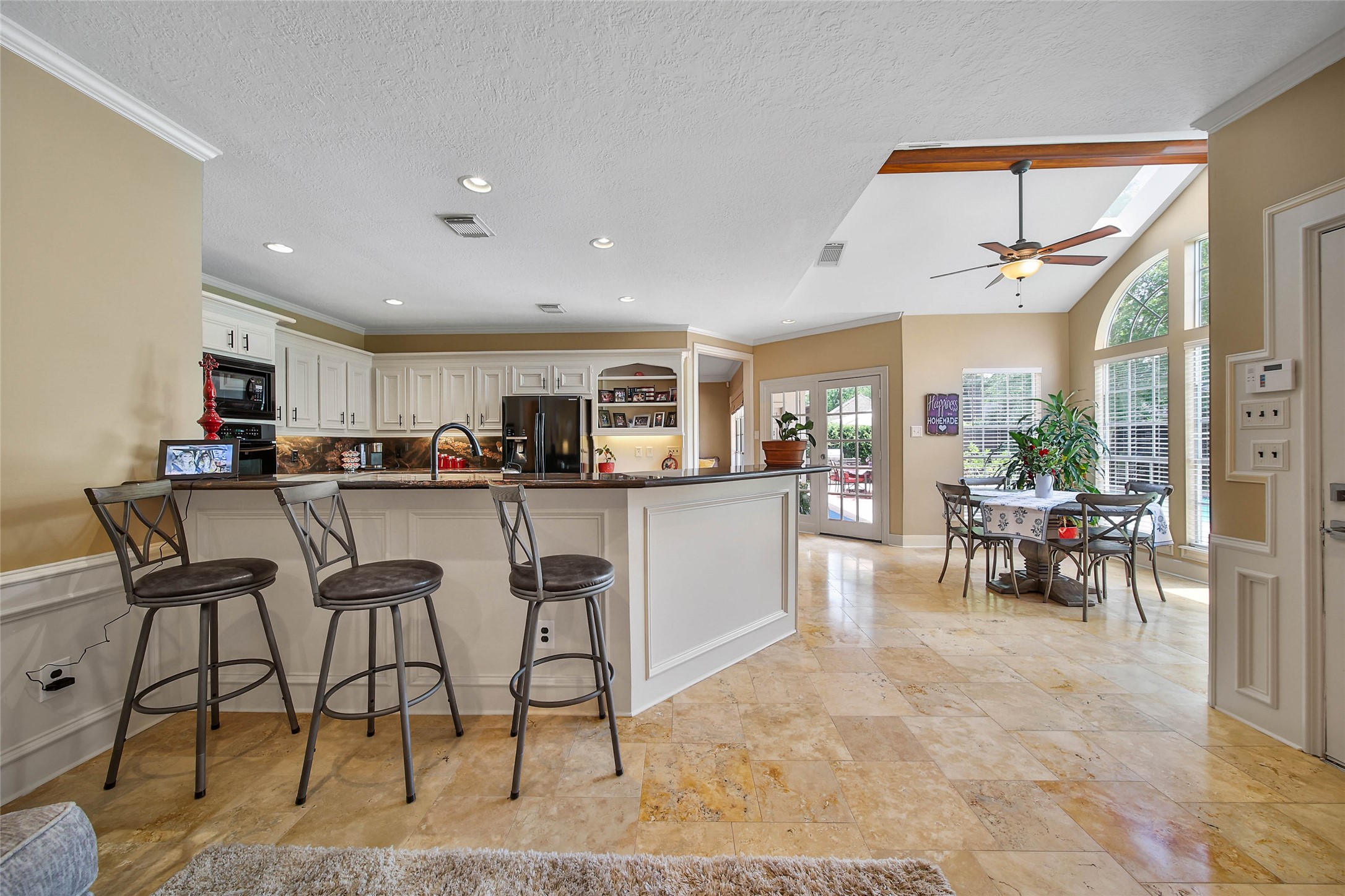This spacious kitchen and dining area features modern appliances, a large island with bar seating, and abundant natural light from large windows. The tiled floor and neutral walls add a touch of elegance, while the open layout is perfect for entertaining.
