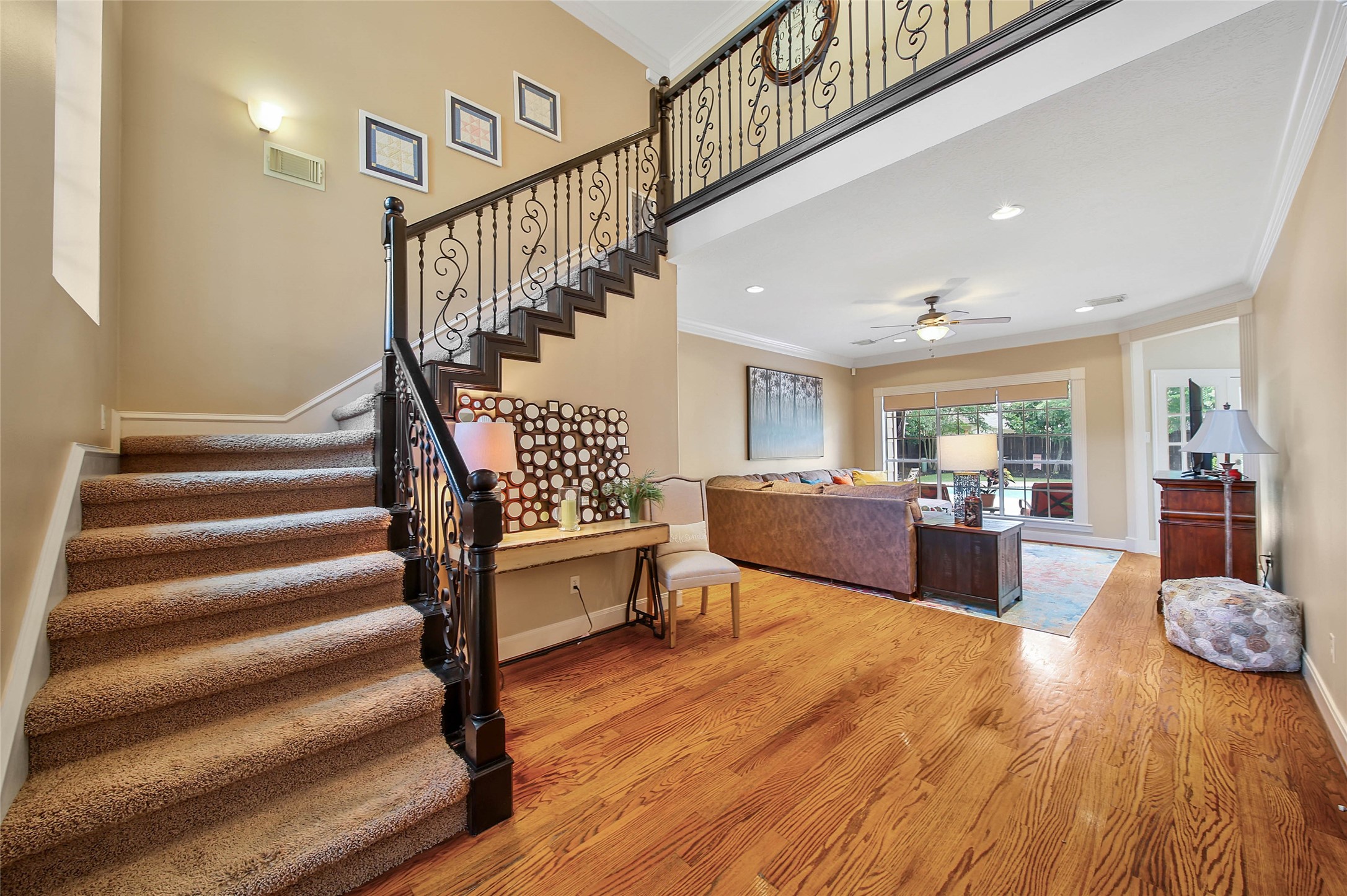 This inviting home features a spacious living area with hardwood floors, a high ceiling, and abundant natural light. The elegant staircase with wrought iron railings adds a touch of sophistication, leading to an open loft area. A large window provides a scenic view of the backyard. Perfect for relaxing and entertaining.