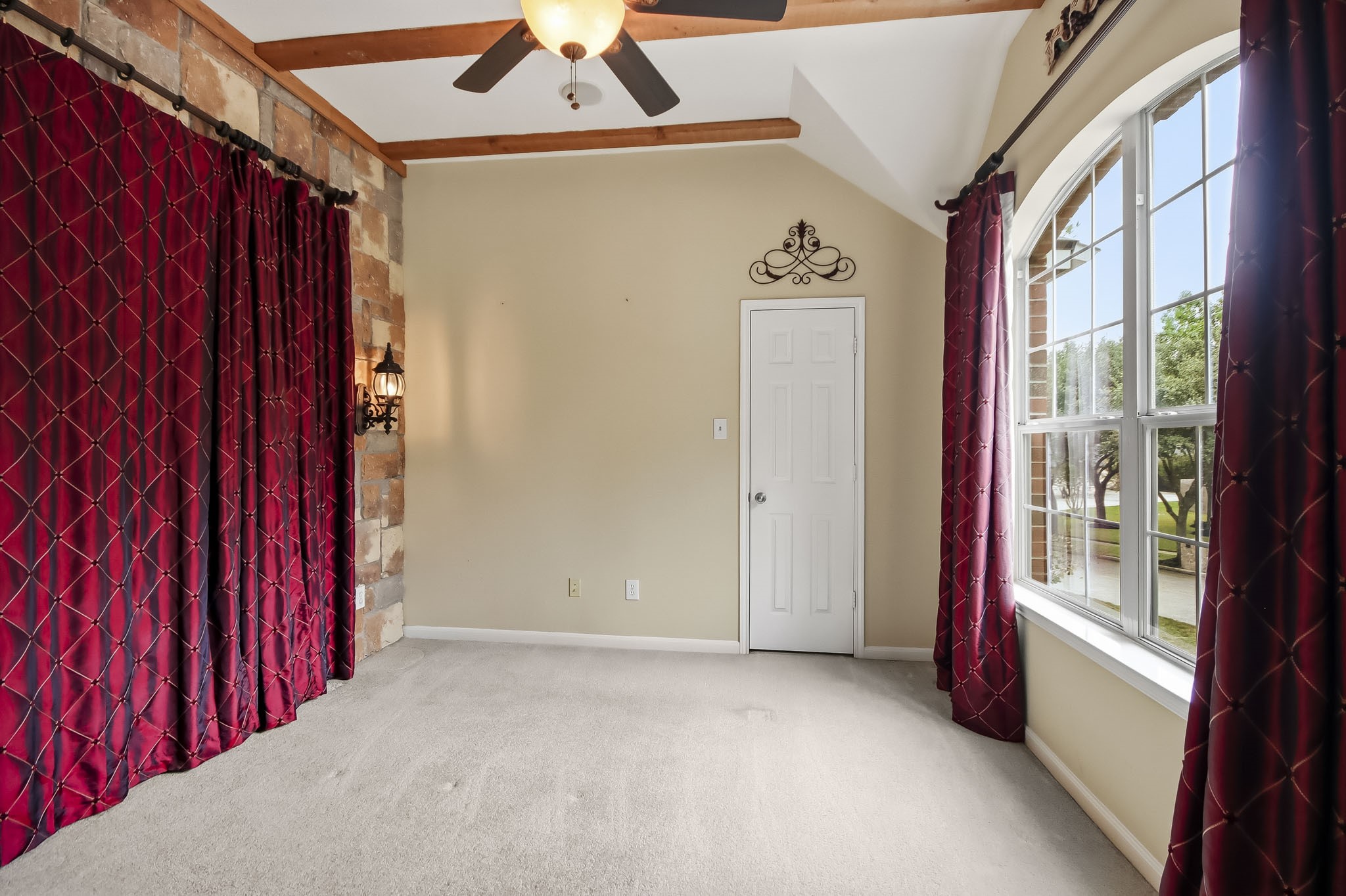 Spacious and versatile room featuring beautiful wood beam ceilings, a decorative stone accent wall, a large arched window with abundant natural light, and a closet. This room offers endless possibilities as a bedroom, home office, media room, or flex space.