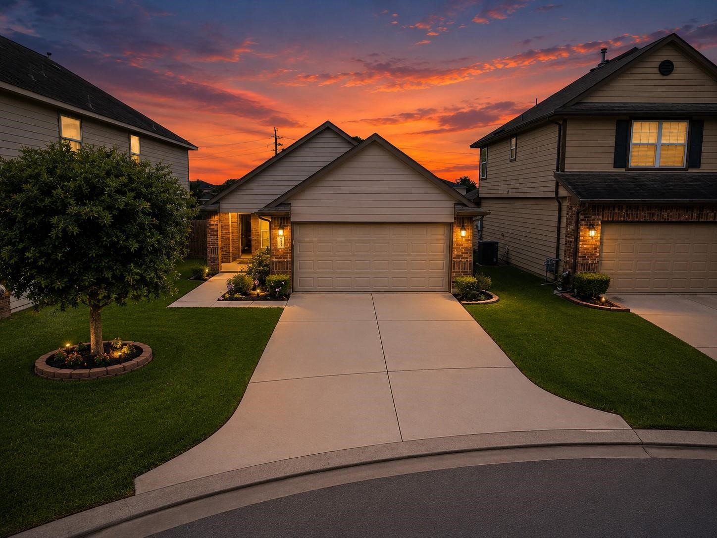 This photo showcases a charming suburban home with a well-maintained front lawn and a two-car garage. The property is beautifully lit with warm exterior lights, and the sunset sky adds a picturesque backdrop.