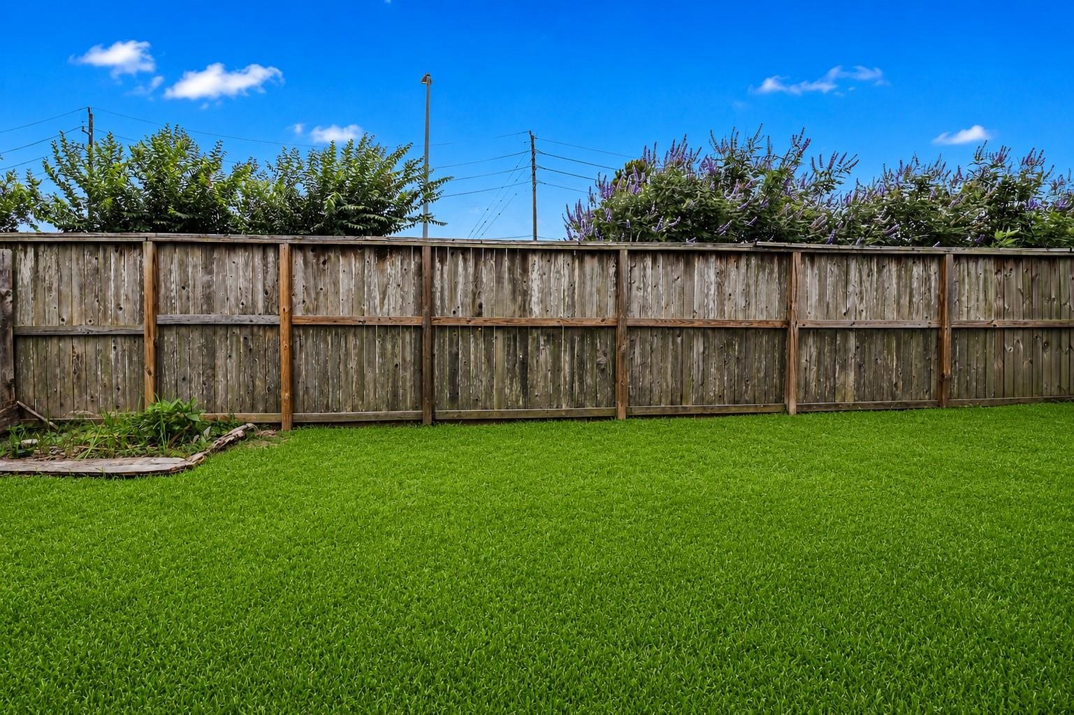 This photo showcases a spacious backyard with lush, green grass enclosed by a wooden fence, providing privacy and a serene outdoor space. The area is ideal for gardening, relaxation, or outdoor activities.