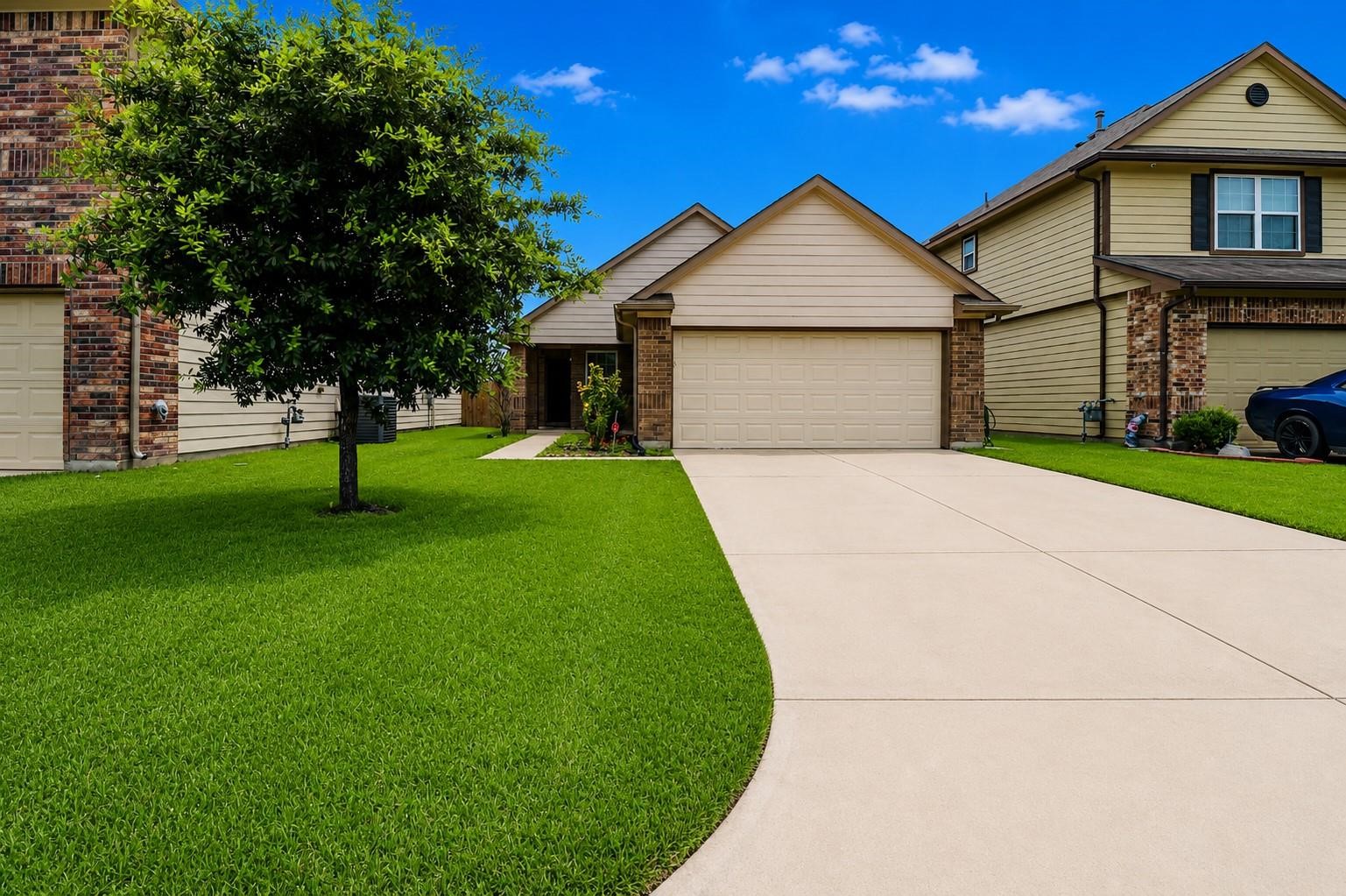 Charming suburban home with a two-car garage, well-maintained lawn, and a mature tree in the front yard. The property features a spacious driveway and is situated in a neighborhood with similar style houses.