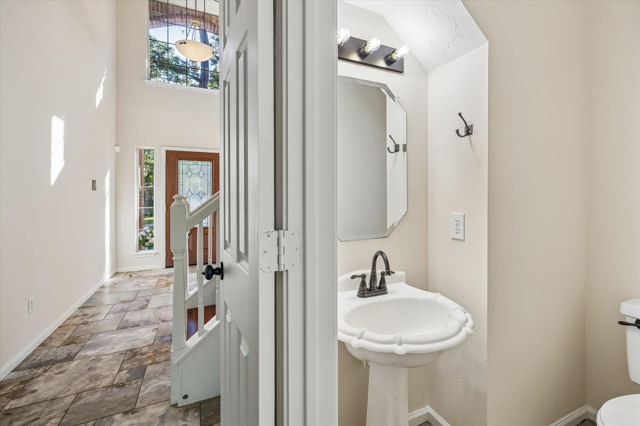 The powder bath is conveniently located just off the entry, offering easy access for guests with a charming pedestal sink and decorative mirror.