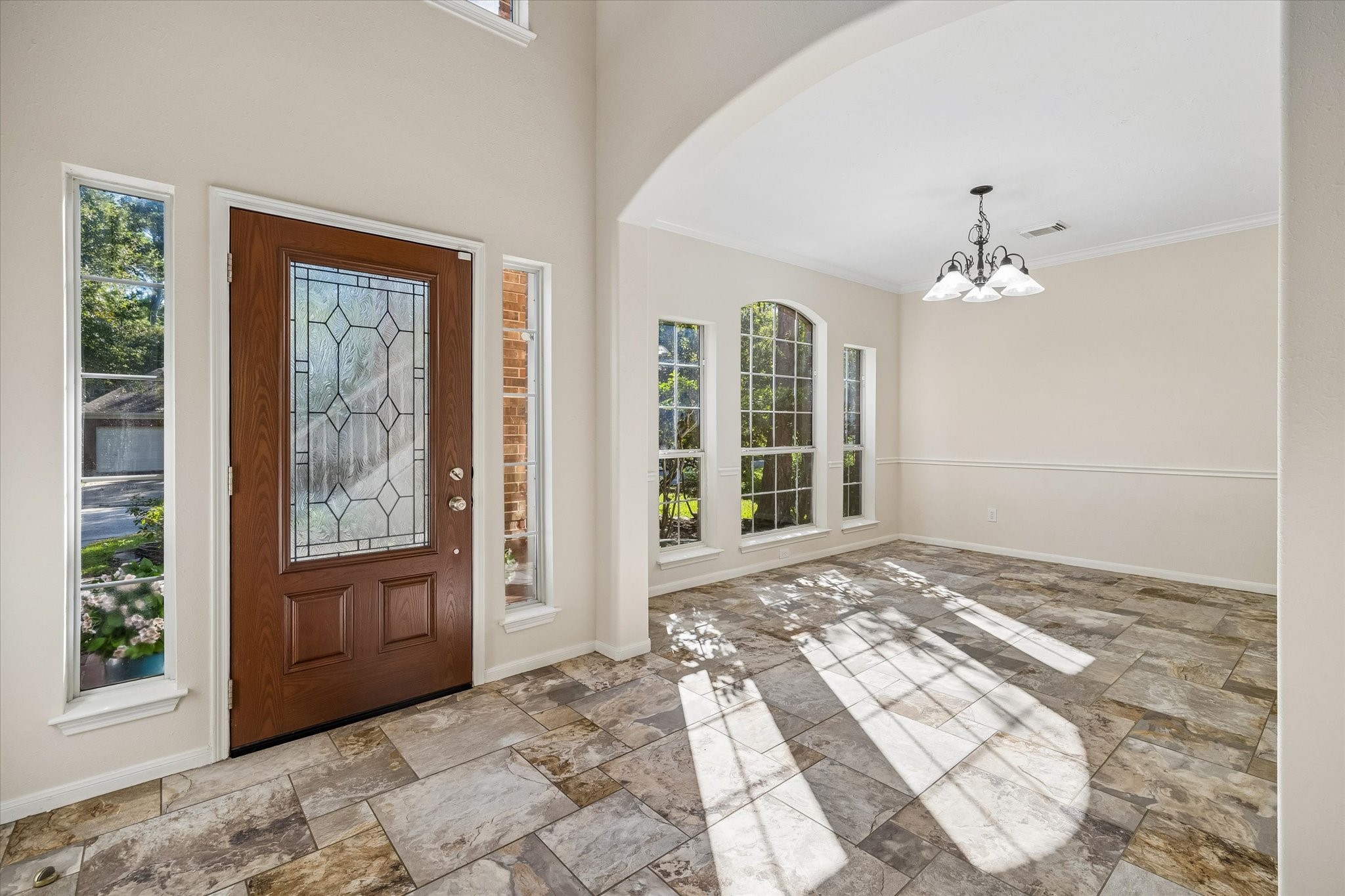 The entry opens into a bright, inviting space with large windows, natural light, and an elegant arched opening leading into the dining area.
