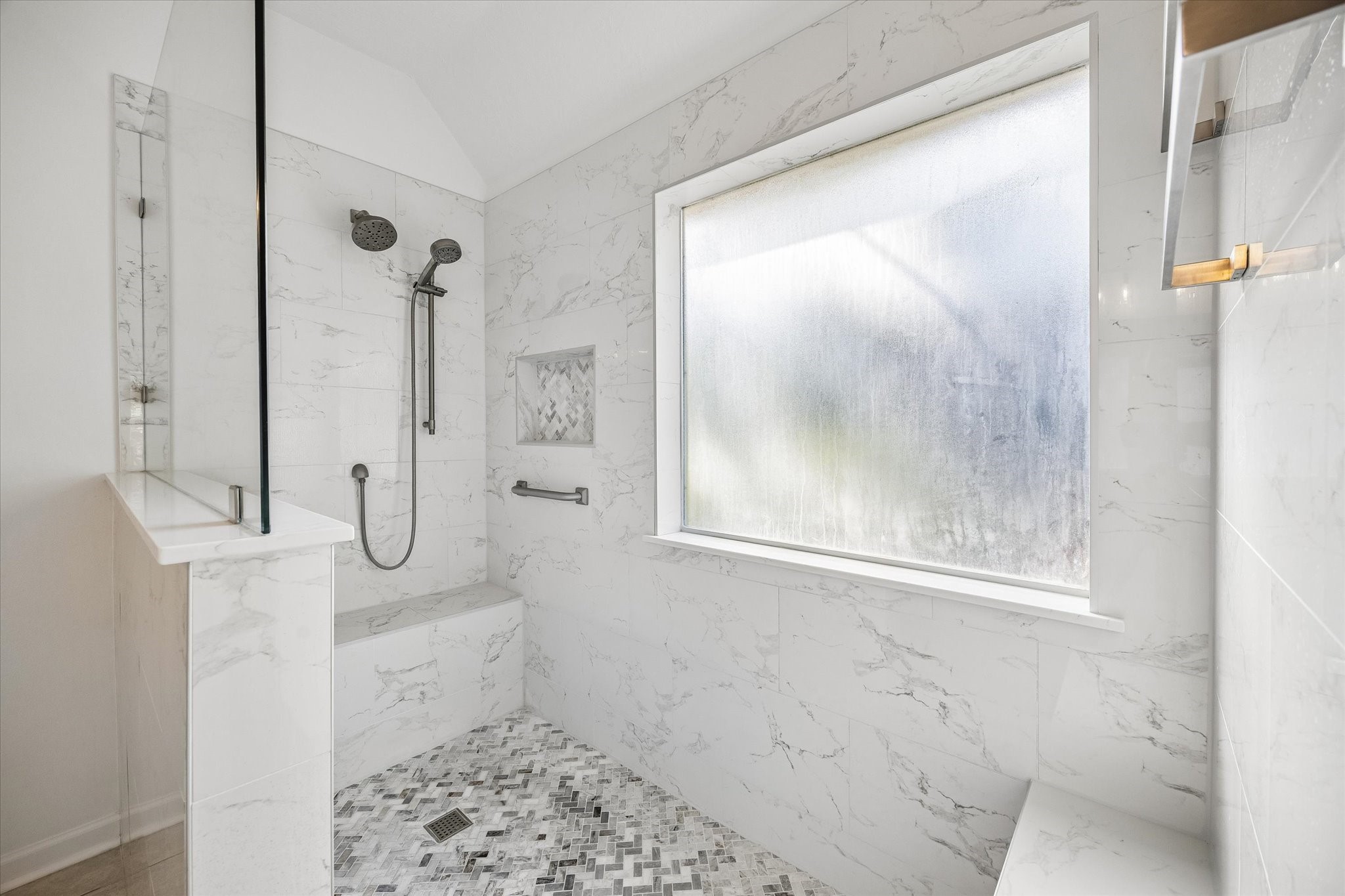 The oversized walk-in shower features decorative mosaic floor, built-in shelving, towel bars, bench, and a sleek glass enclosure!