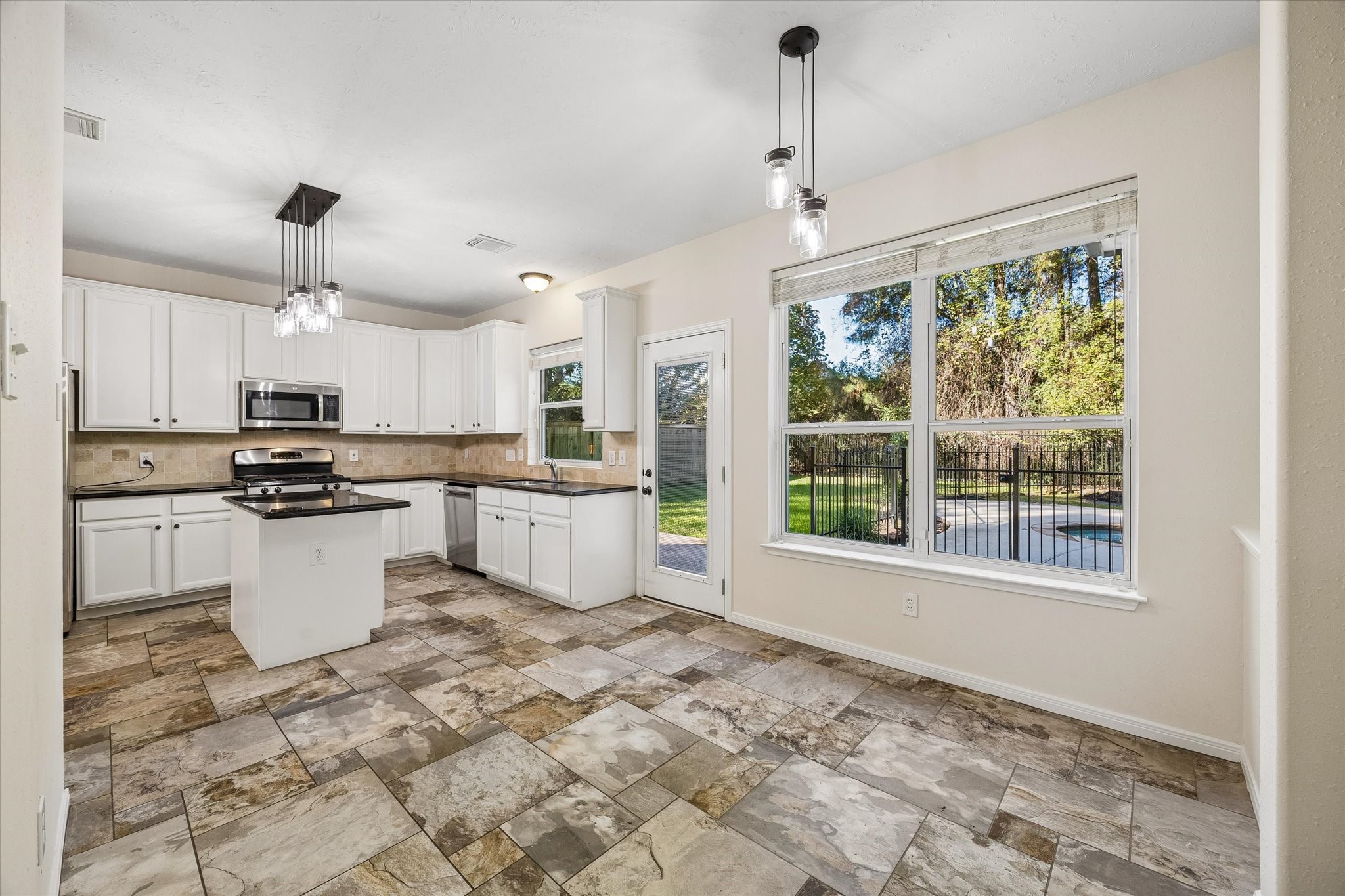 The kitchen flows seamlessly into the breakfast area, where large windows fill the space with natural light and offer lovely views of the sparkling pool and backyard.