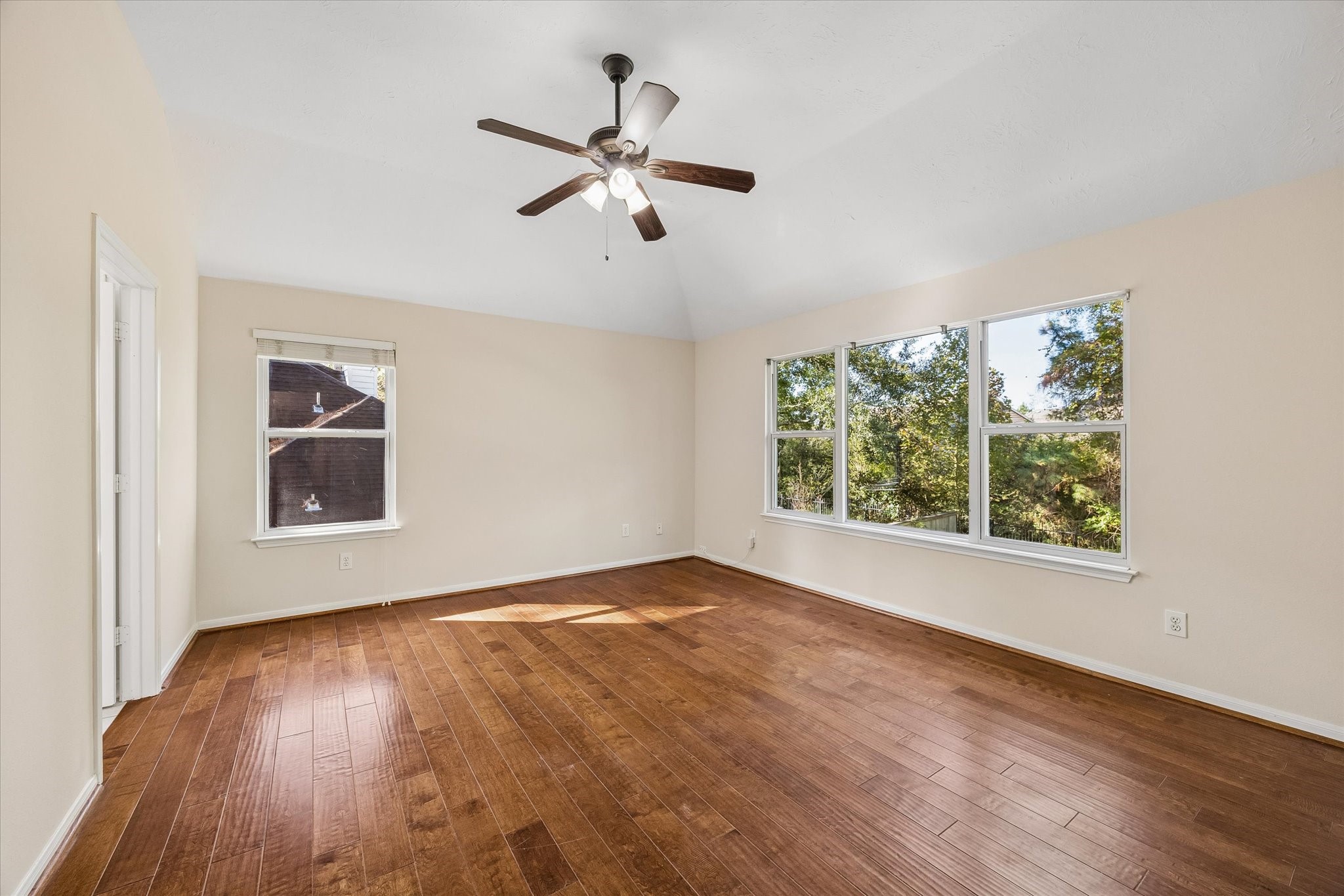 Spacious second-level primary bedroom featuring engineered wood flooring and expansive windows that fill the room with natural light while offering peaceful views of the surrounding greenery.