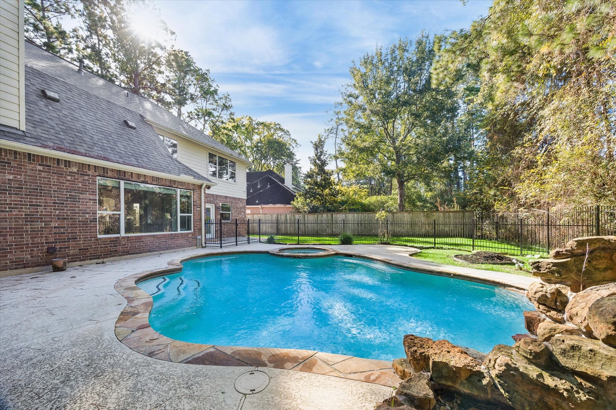 Another view of the beautiful pool and spa, surrounded by a spacious patio and mature trees! The pool has been resurfaced with a pebble tec finish and features a heater and child safe fence.