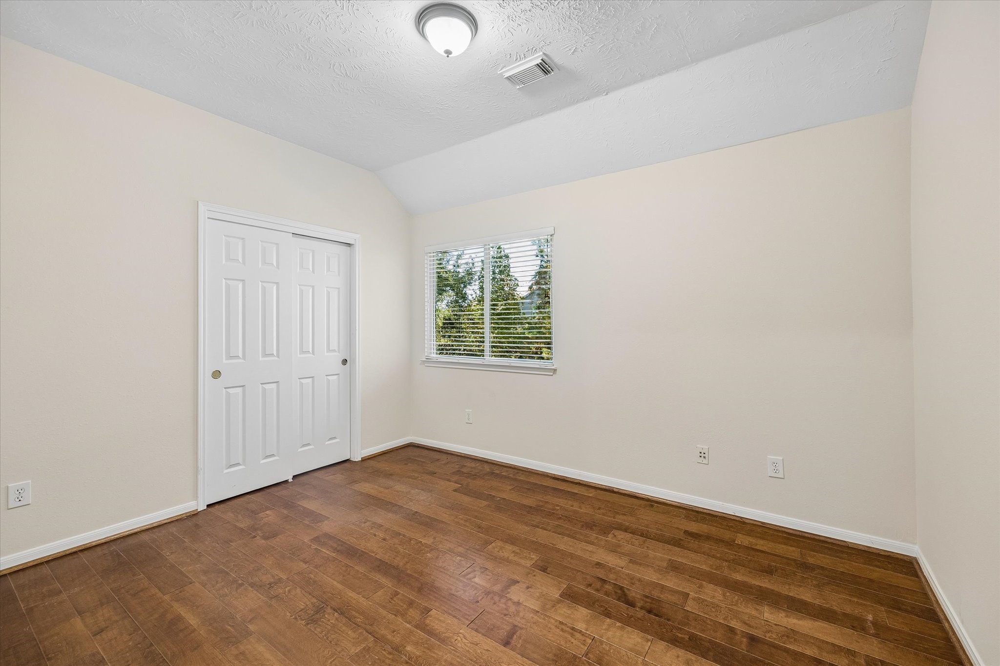 The secondary bedroom features warm wood flooring, adding a rich touch of character while complementing the neutral walls and filling the space with a bright, inviting feel.