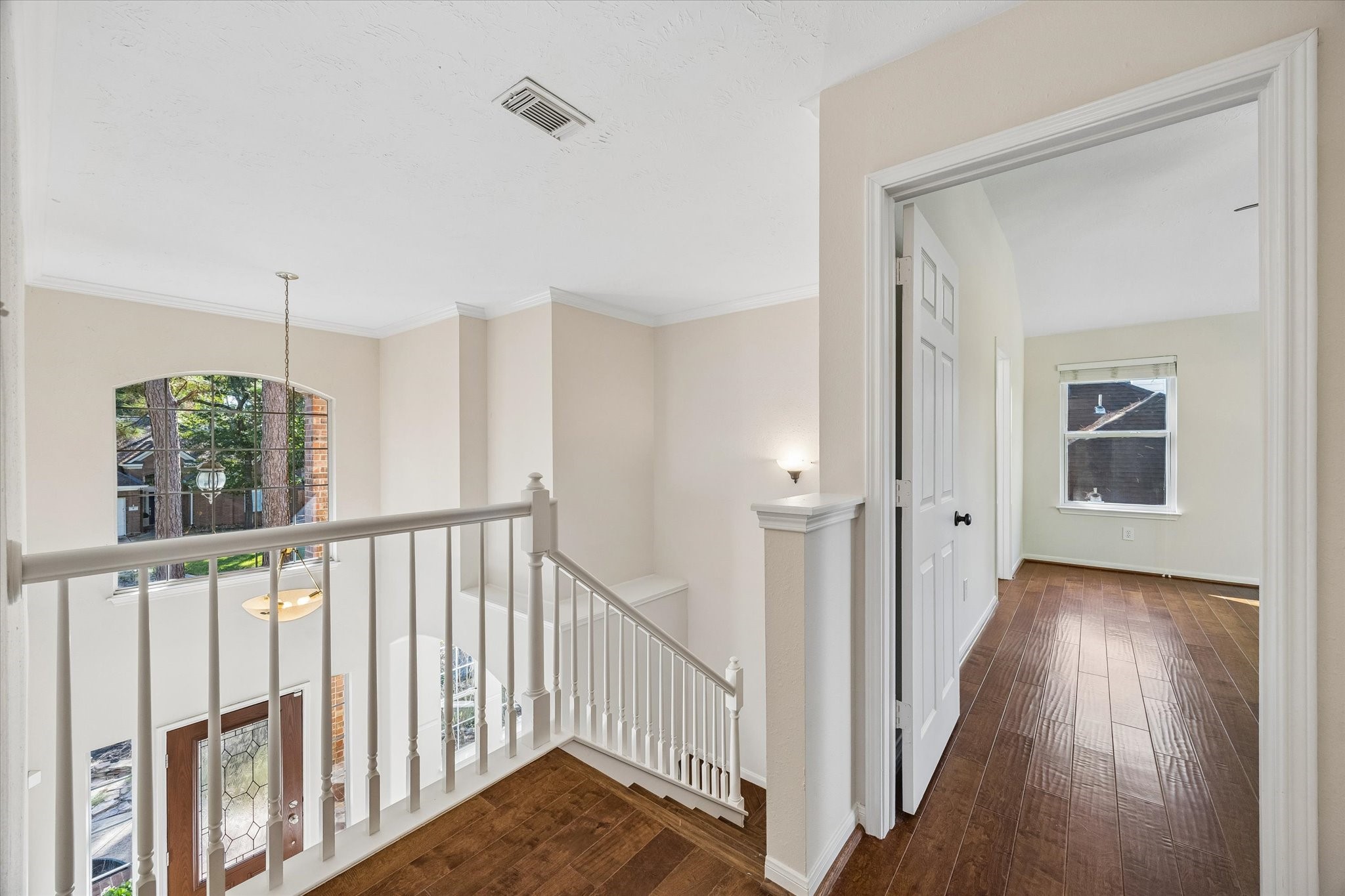 The upstairs landing overlooks the entryway below, creating an open, airy feel, while the warm wood flooring continues down the hallway to the secondary bedrooms.