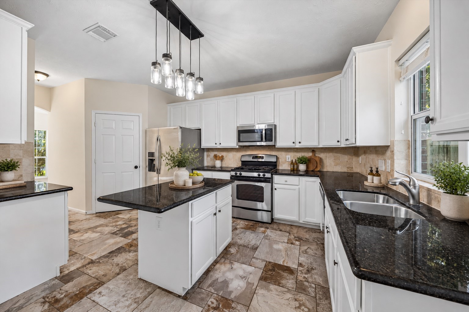 The kitchen features crisp white cabinetry, sleek black granite countertops, and stainless steel appliances. A center island provides additional prep space! Virtually staged with accessories.