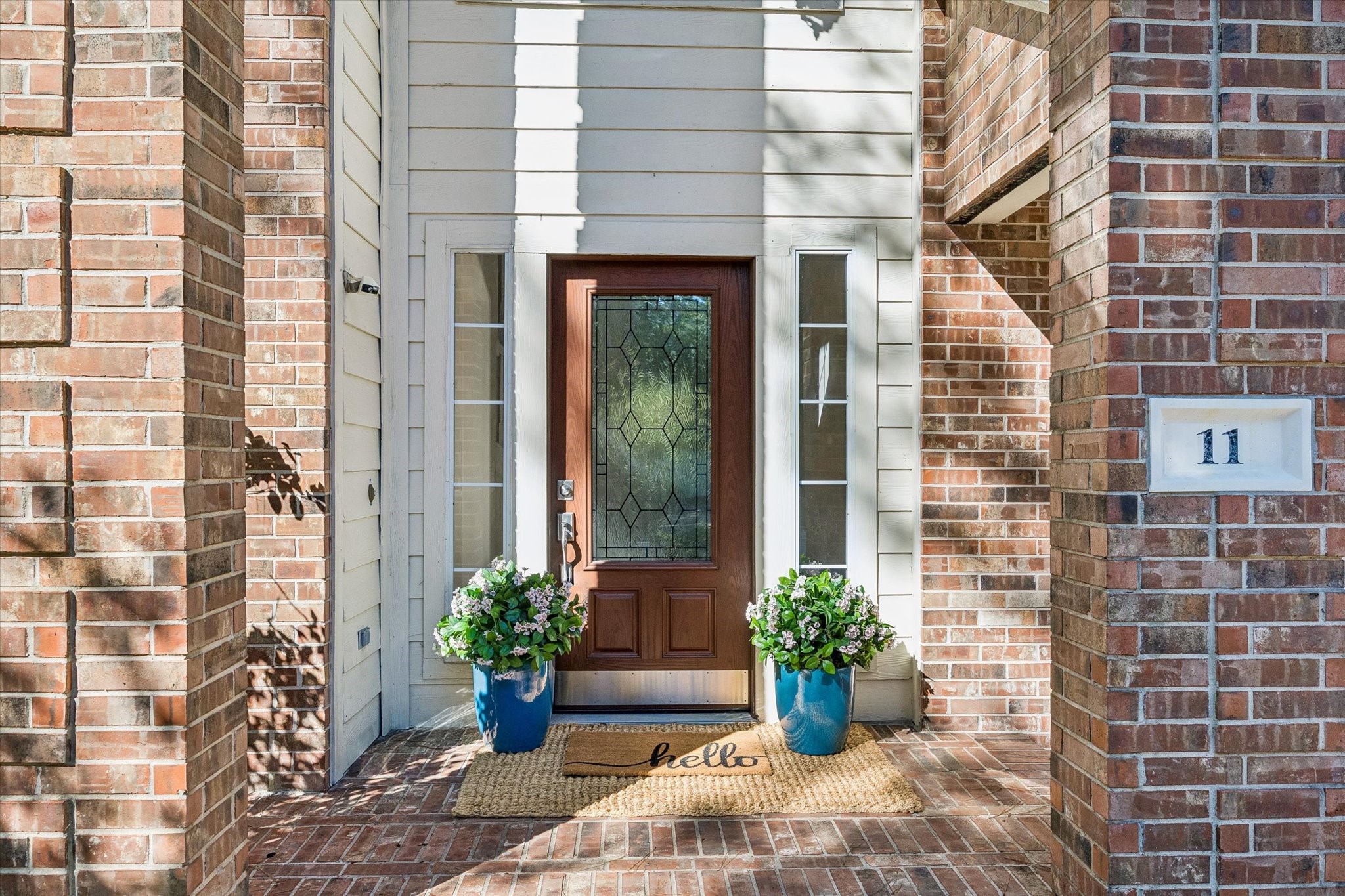 Step inside through the welcoming entryway, featuring a beautiful custom wood front door with decorative glass, framed by classic brick accents.