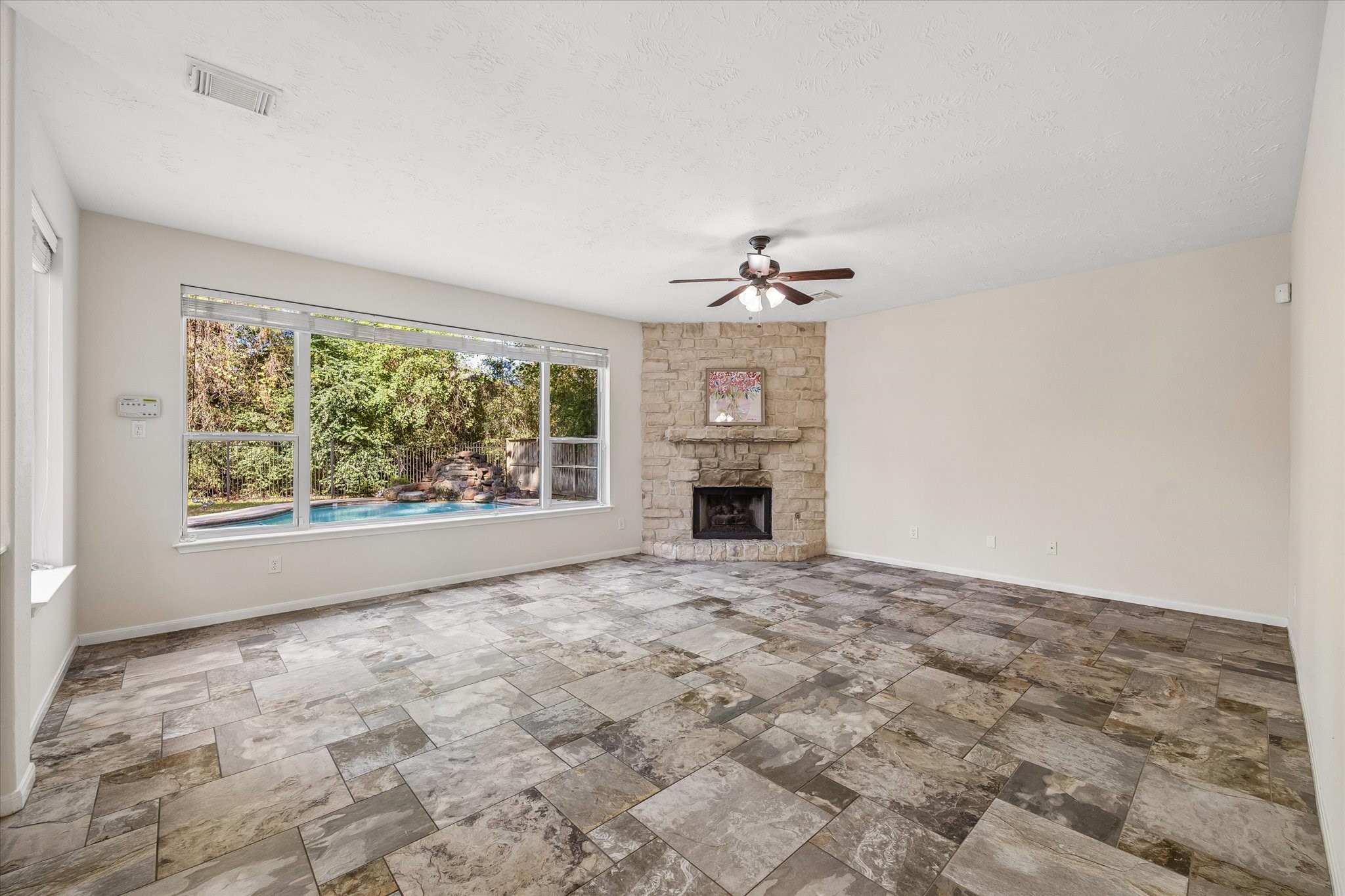 Spacious living area featuring a beautiful stone fireplace, expansive windows overlooking the backyard and pool, and an abundance of natural light. Floors and light fixtures have been updated in this home!