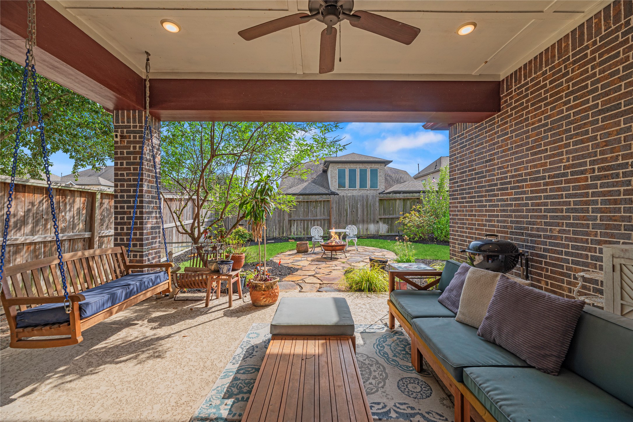 Attractive covered patio with cozy swing and landscaping.