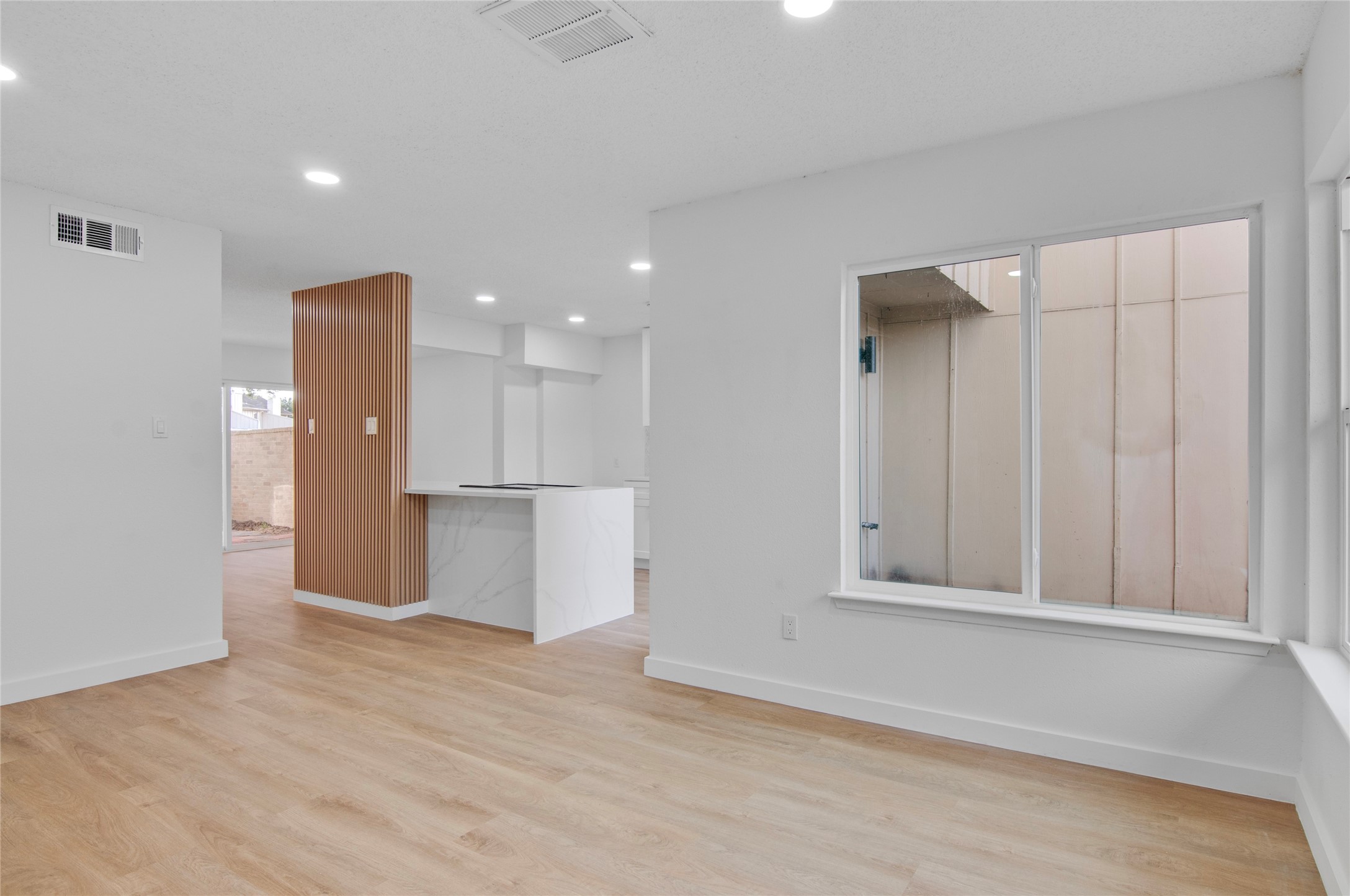 Bright, open living space featuring sleek wood flooring and a modern kitchen island with white cabinetry, complemented by ample natural light from large windows.