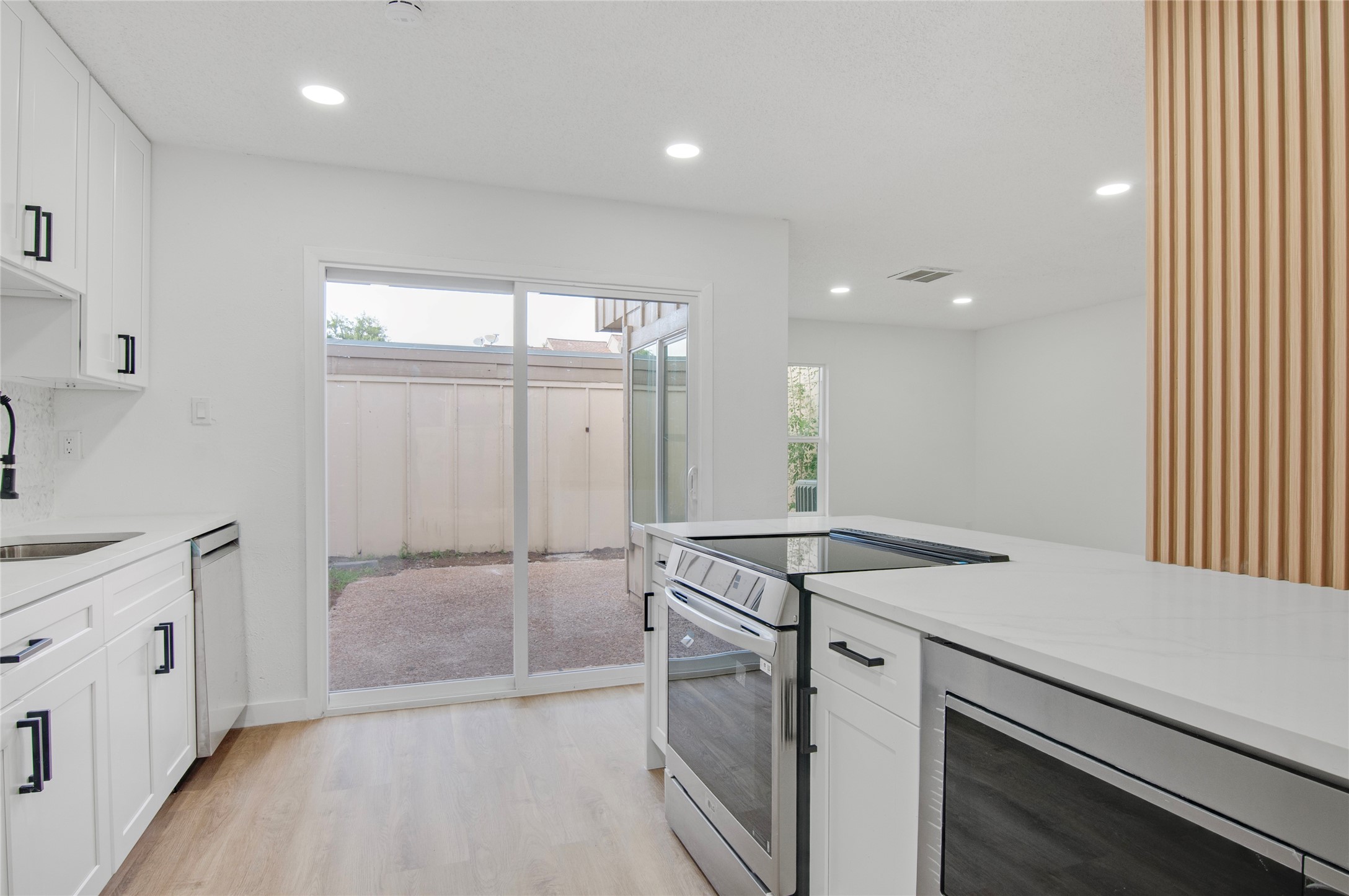 Bright and modern kitchen with sleek appliances, white cabinetry, and a large sliding glass door leading to a private outdoor space.