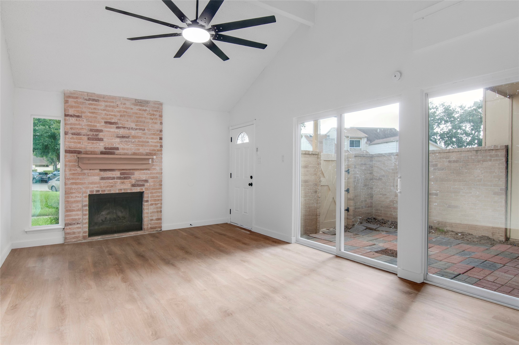 Bright living space featuring a vaulted ceiling, cozy brick fireplace, and new large sliding glass doors leading to a private patio.