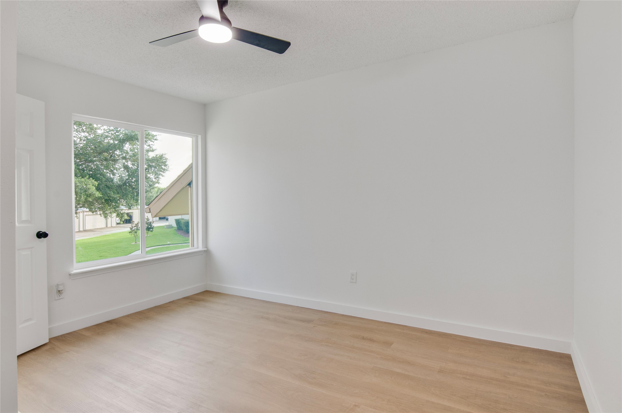Bright and airy room featuring sleek laminate flooring, a modern ceiling fan, and a large window with a serene view of lush greenery.