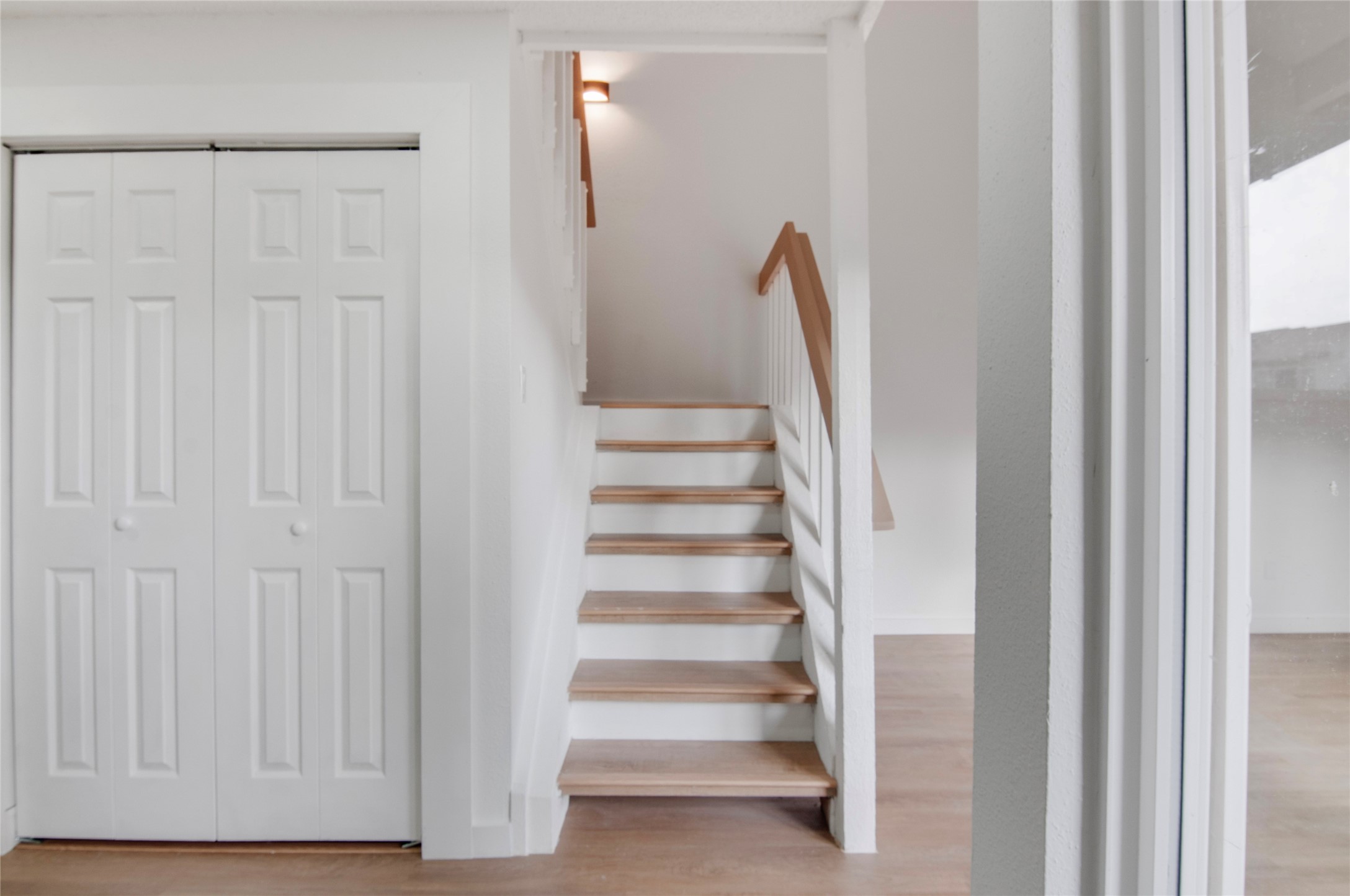 Bright and inviting staircase with elegant wood accents leads to the upper level, alongside a convenient closet with double doors, perfect for storage.