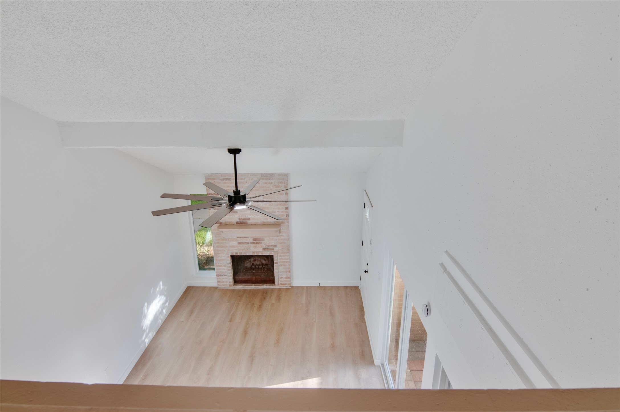 Spacious living area with a charming brick fireplace, sleek ceiling fan, and abundant natural light from large windows.