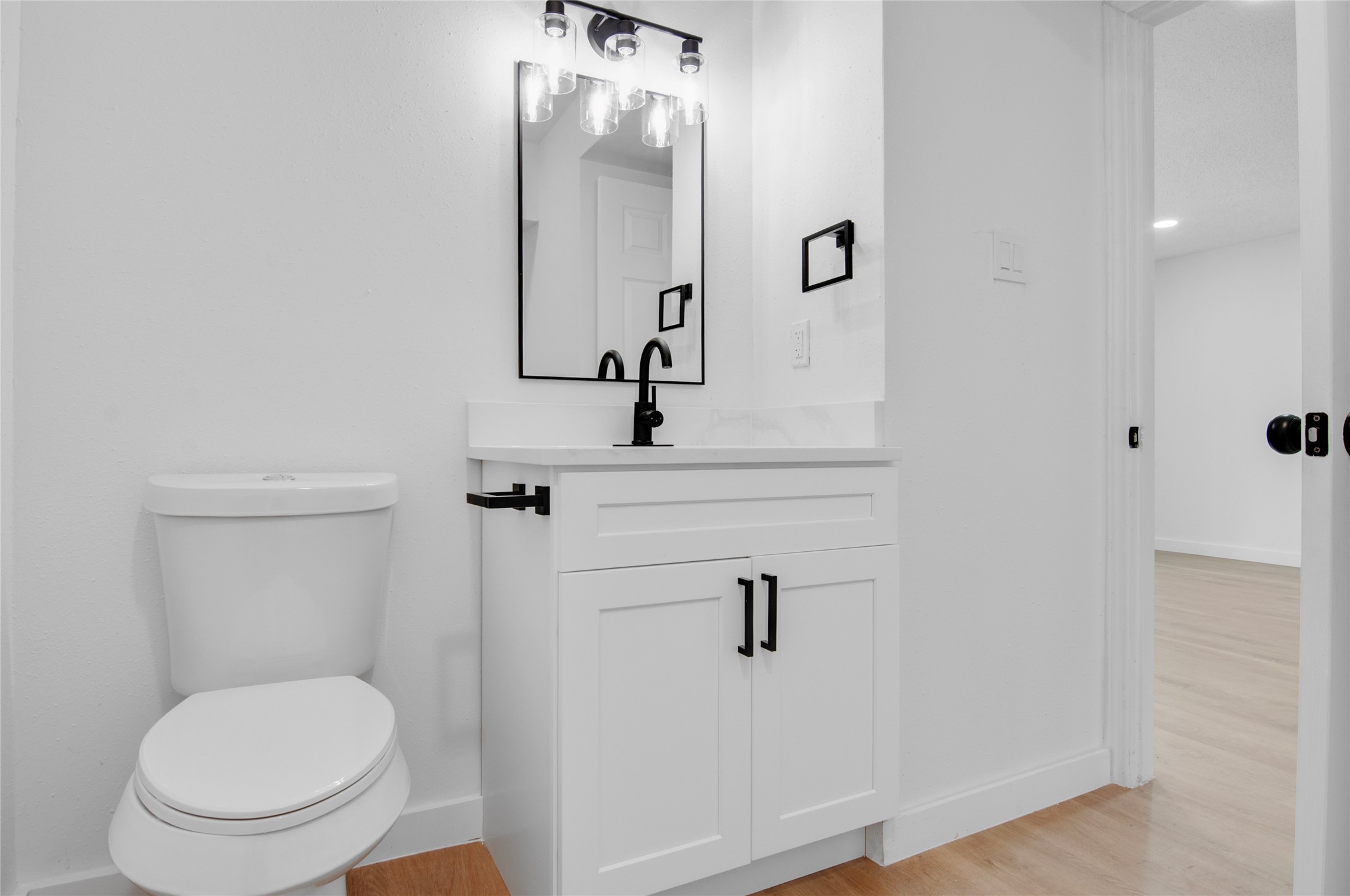 Stylish bathroom with a modern vanity featuring sleek black fixtures, a framed mirror, and pristine white cabinetry, complemented by light wood flooring.
