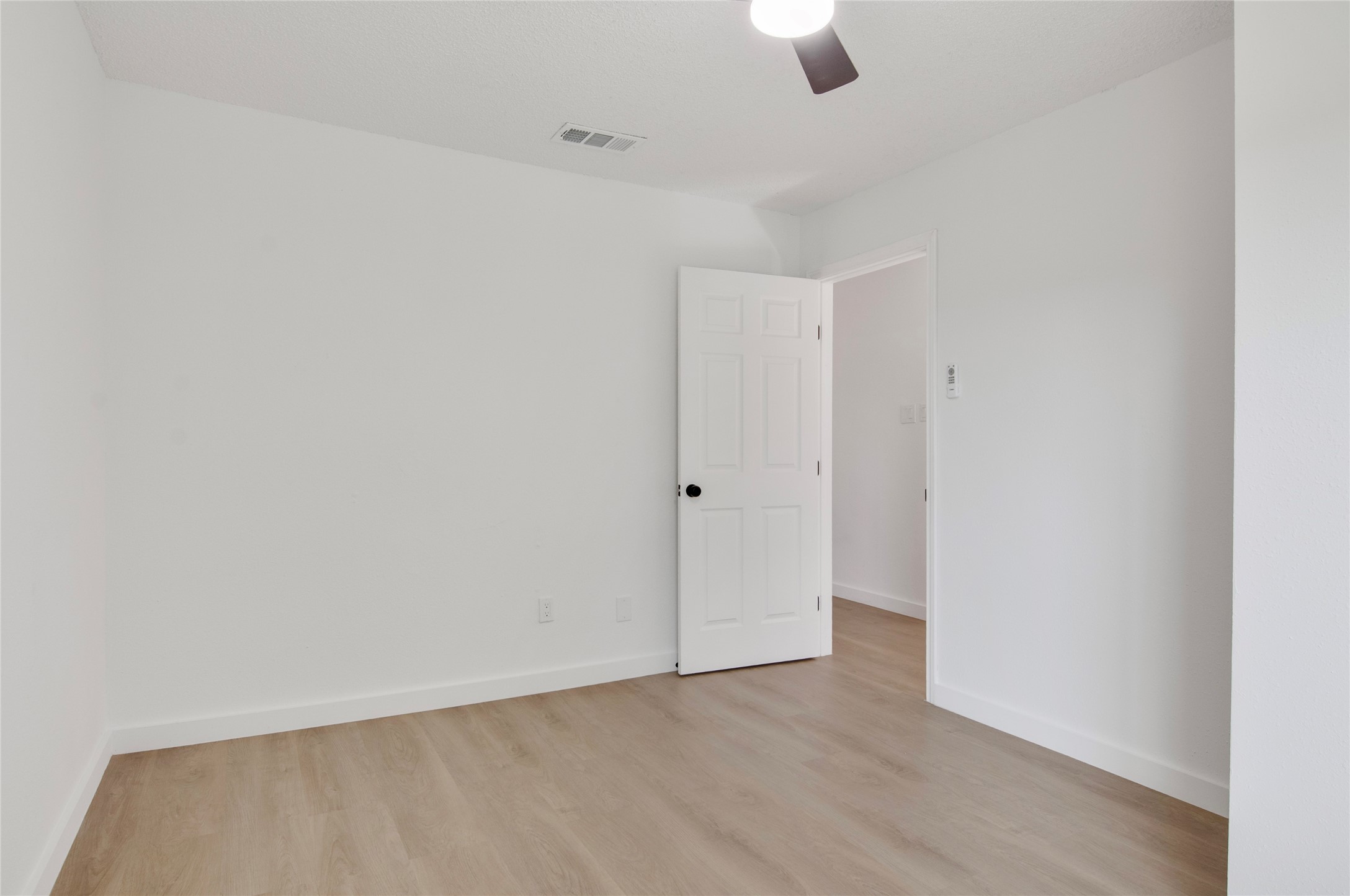 Bright, minimalist room featuring fresh white walls and sleek wood flooring, complemented by a modern ceiling fan.