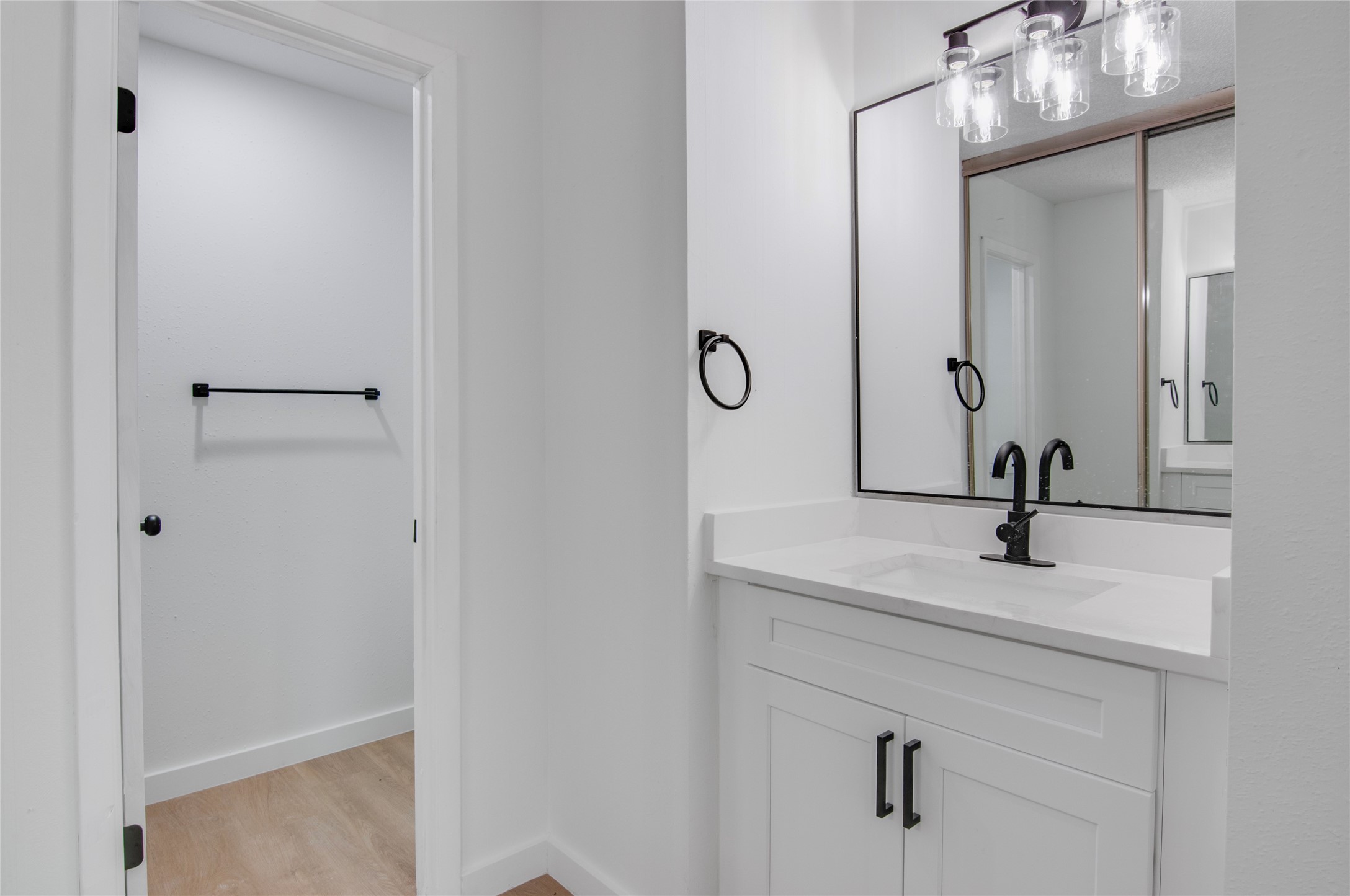 Sleek and modern bathroom features a stylish vanity with a black faucet, large framed mirror, and ample lighting, leading to a spacious walk-in closet.