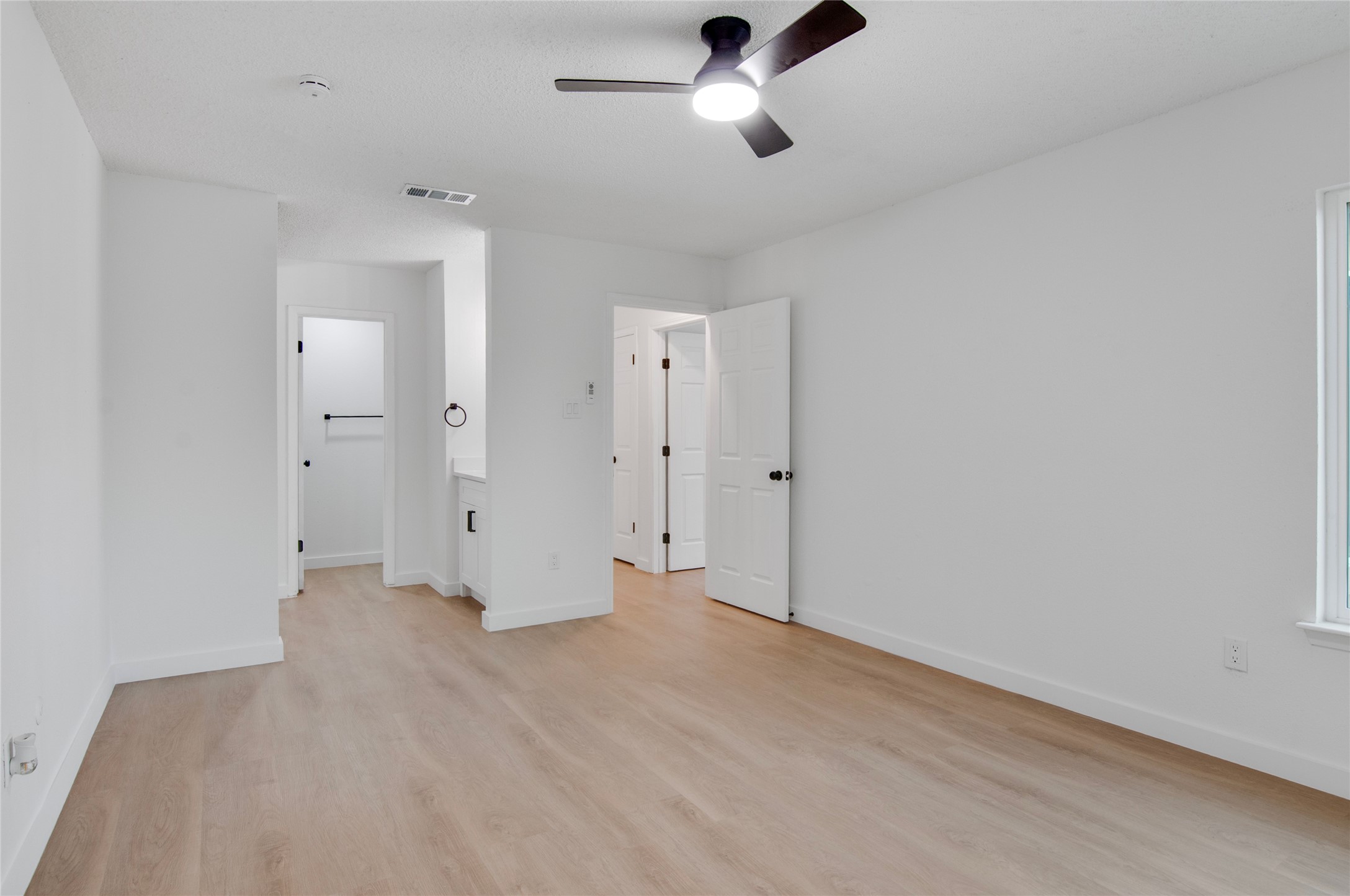 Spacious bedroom with sleek laminate flooring, modern ceiling fan, and ample natural light, featuring an en-suite bathroom and walk-in closet.