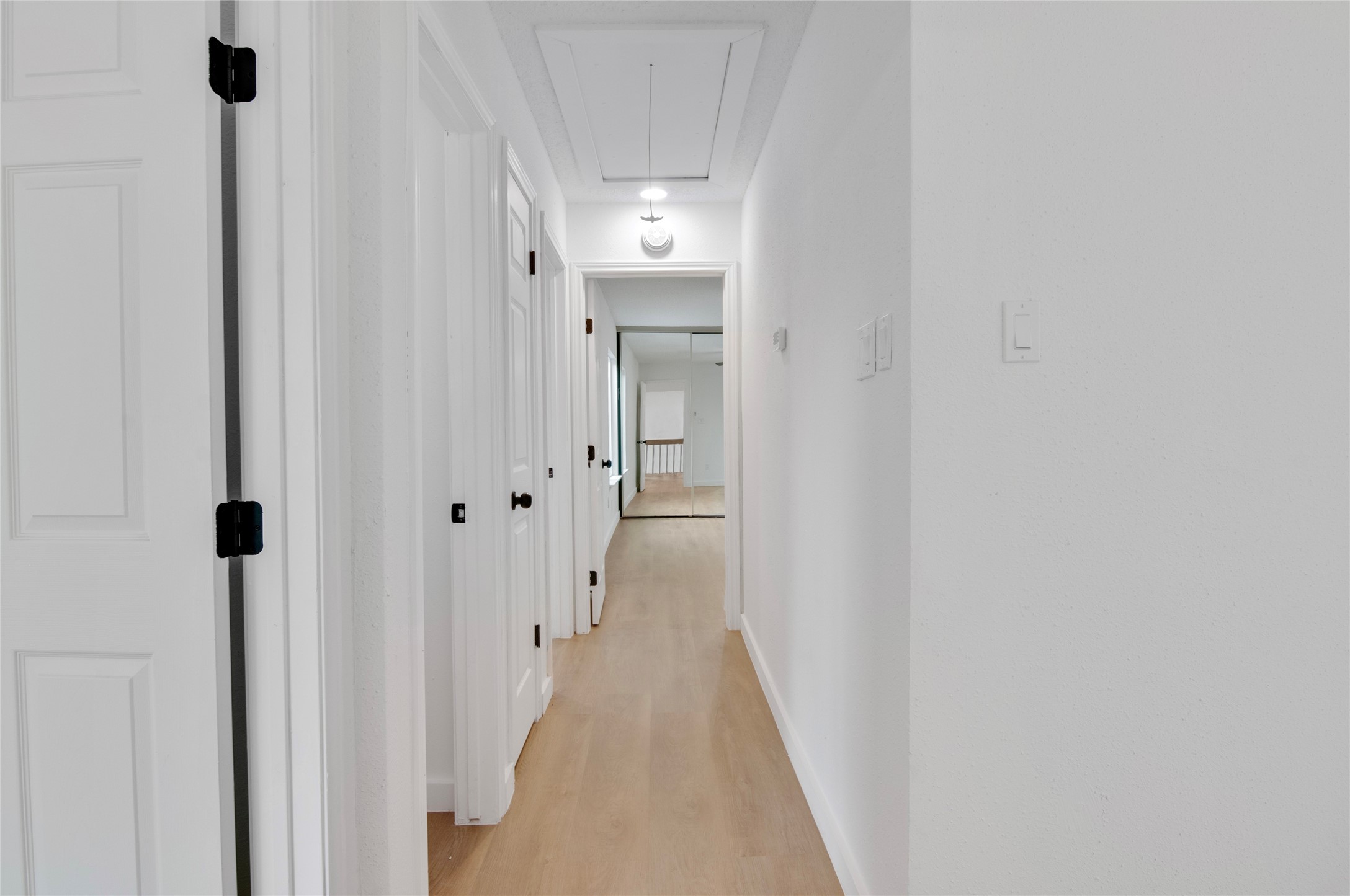 Bright and inviting hallway with light wood flooring and crisp white walls, leading to multiple rooms for easy access and flow.