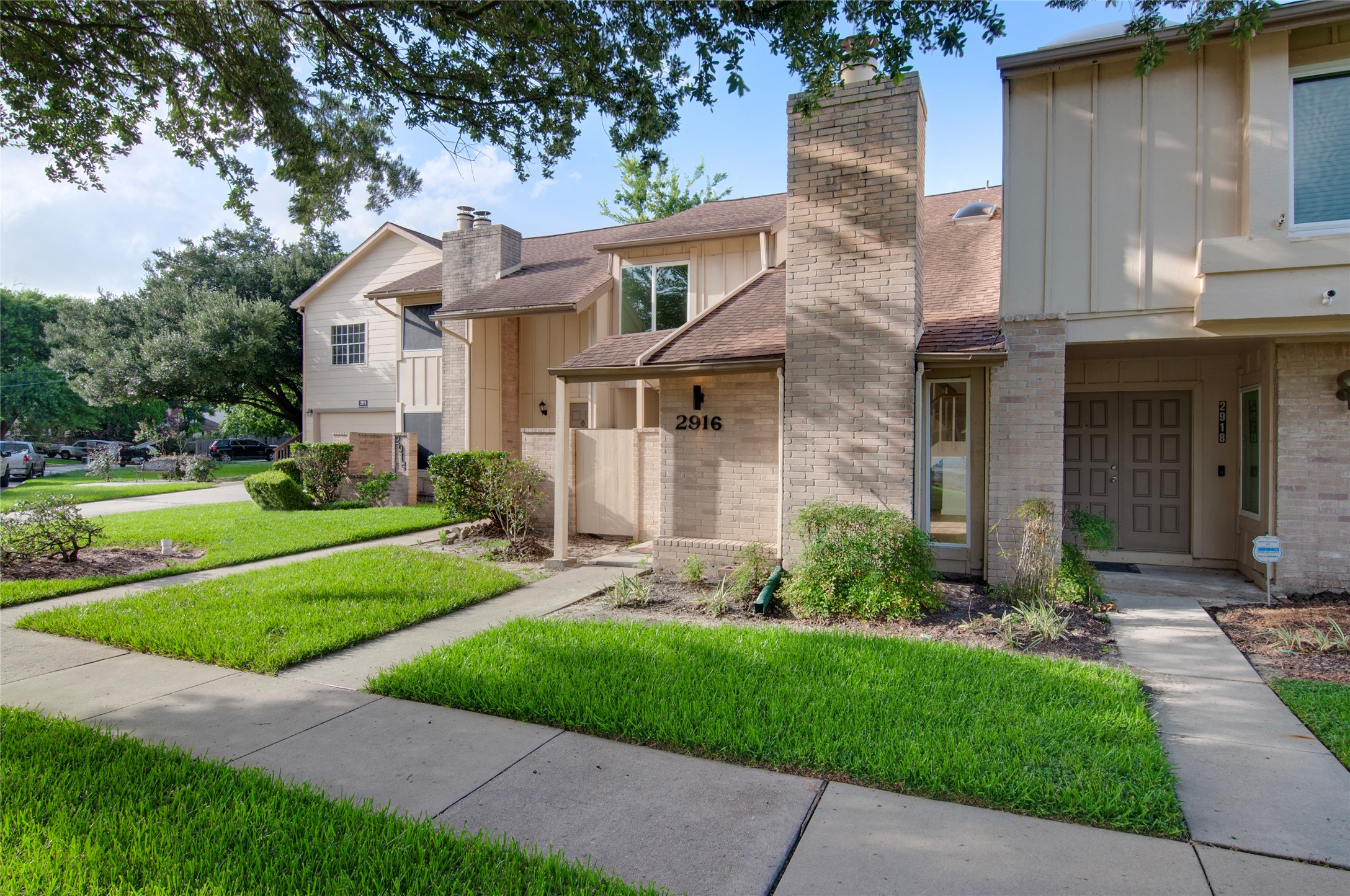 Charming townhouse with a welcoming brick exterior and lush, manicured landscaping, nestled in a serene neighborhood setting.