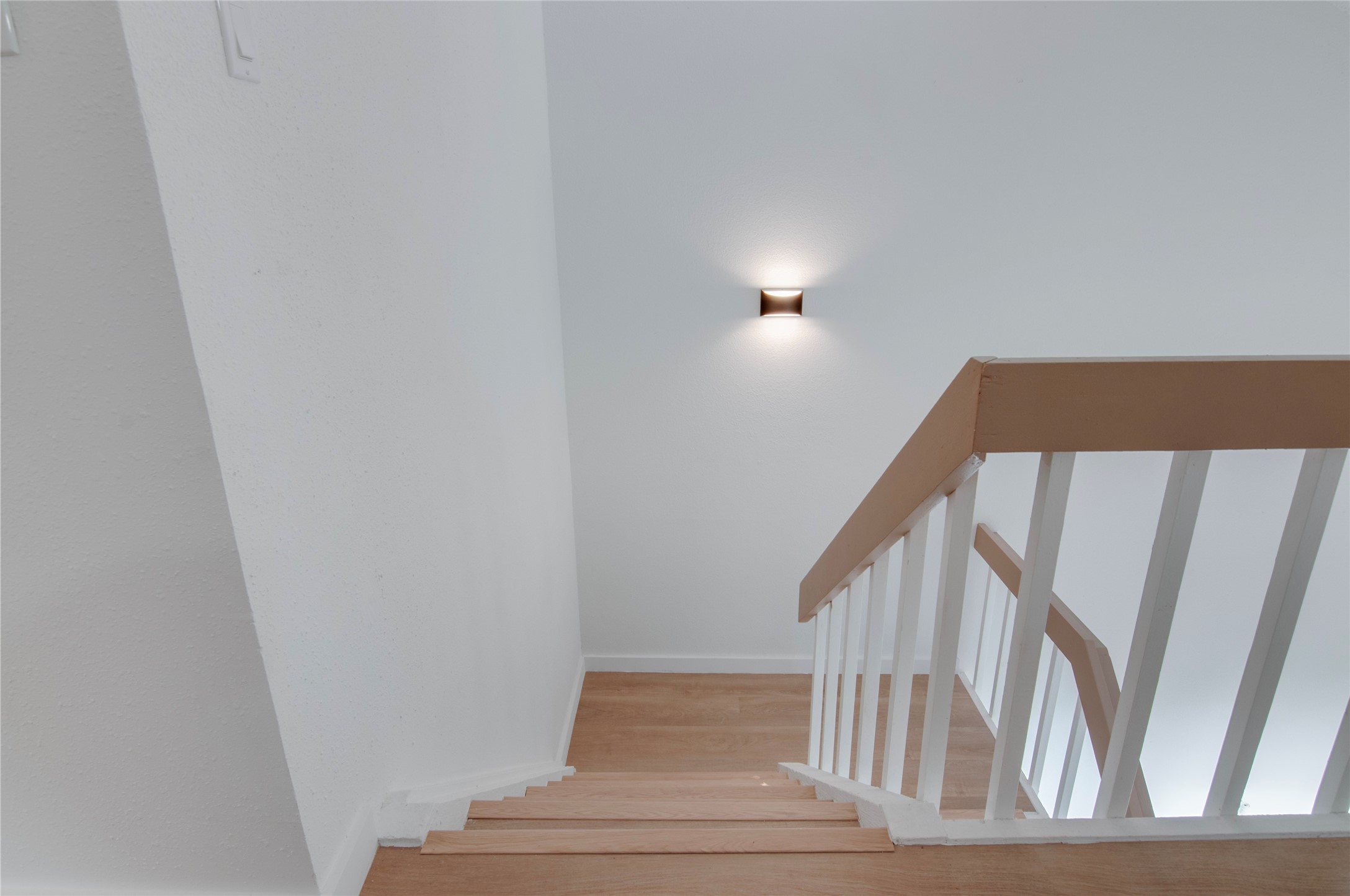 Modern staircase with sleek wooden steps and white railing, enhanced by a stylish wall-mounted light fixture.