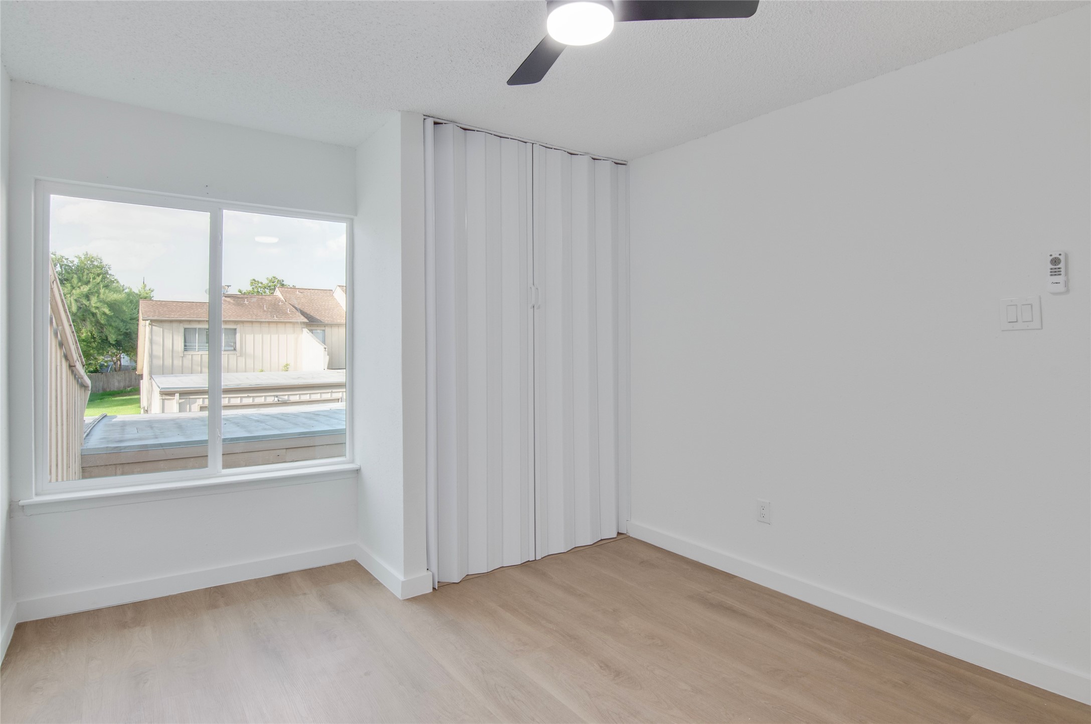 Bright and airy room with large window, sleek ceiling fan, and modern laminate flooring, perfect for a cozy living space.