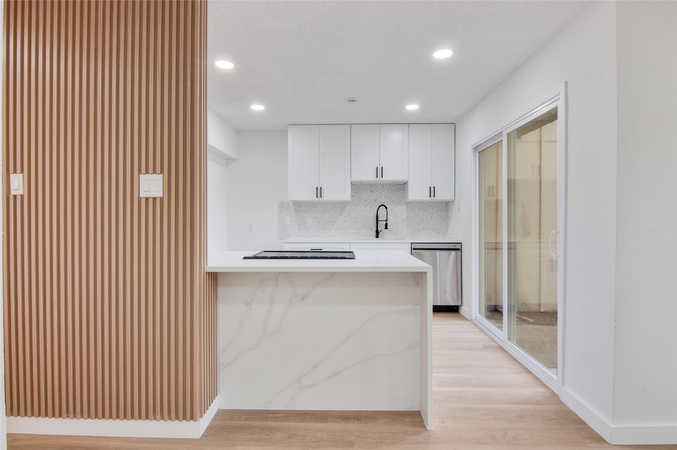 Modern kitchen featuring sleek cabinetry, a stylish island with marble accents, and stainless steel appliances, enhanced by natural light from sliding glass doors.