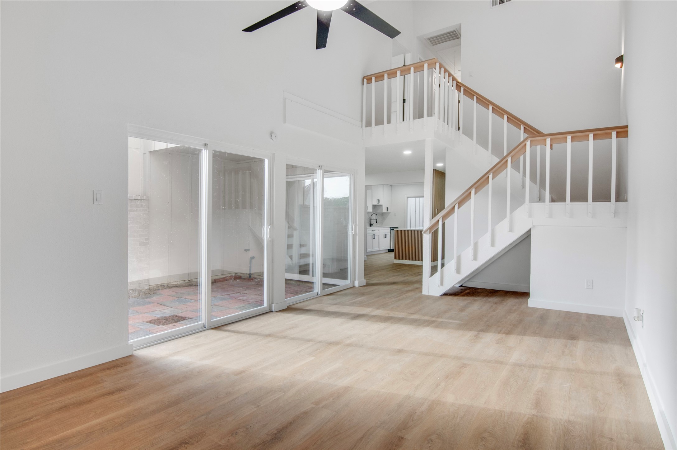 Spacious living area with high ceilings, abundant natural light from large glass doors, and an elegant staircase leading to the upper level.
