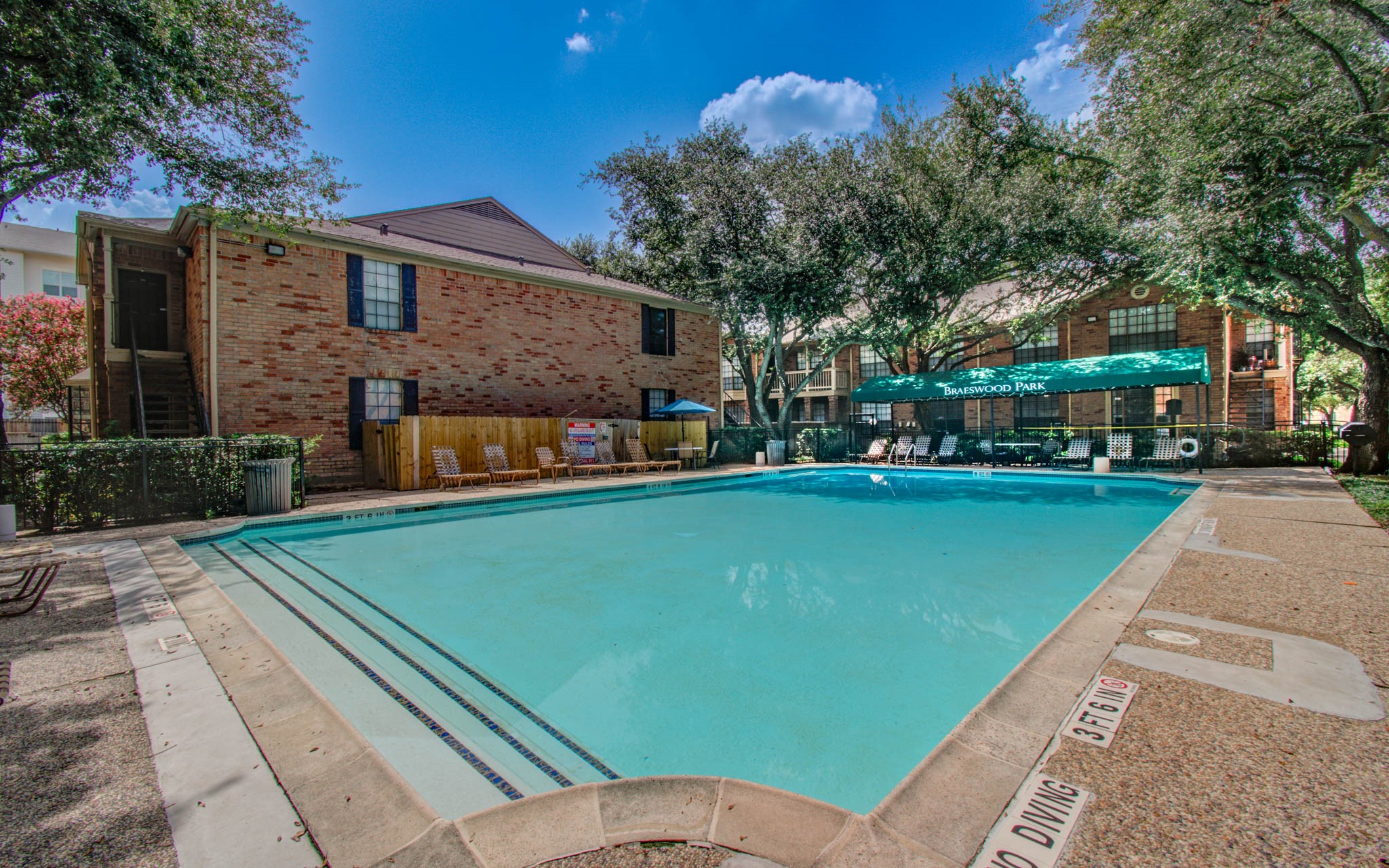 This photo showcases a community swimming pool surrounded by trees, featuring a shaded area with lounge chairs, perfect for relaxation and outdoor enjoyment.