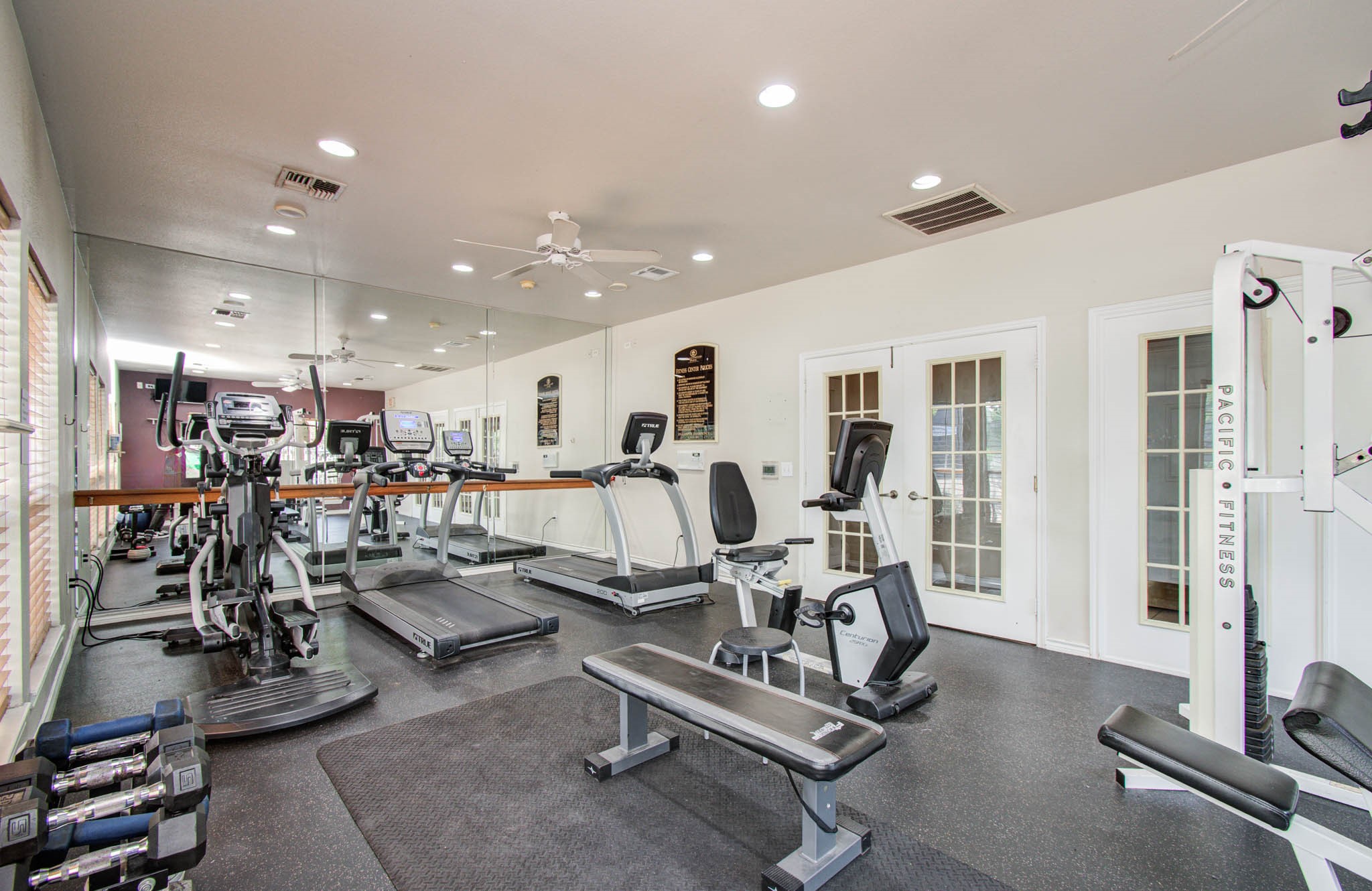 Well-equipped home gym with treadmills, exercise bikes, weights, and strength machines. It features mirrored walls, bright lighting, and a clean, spacious layout.