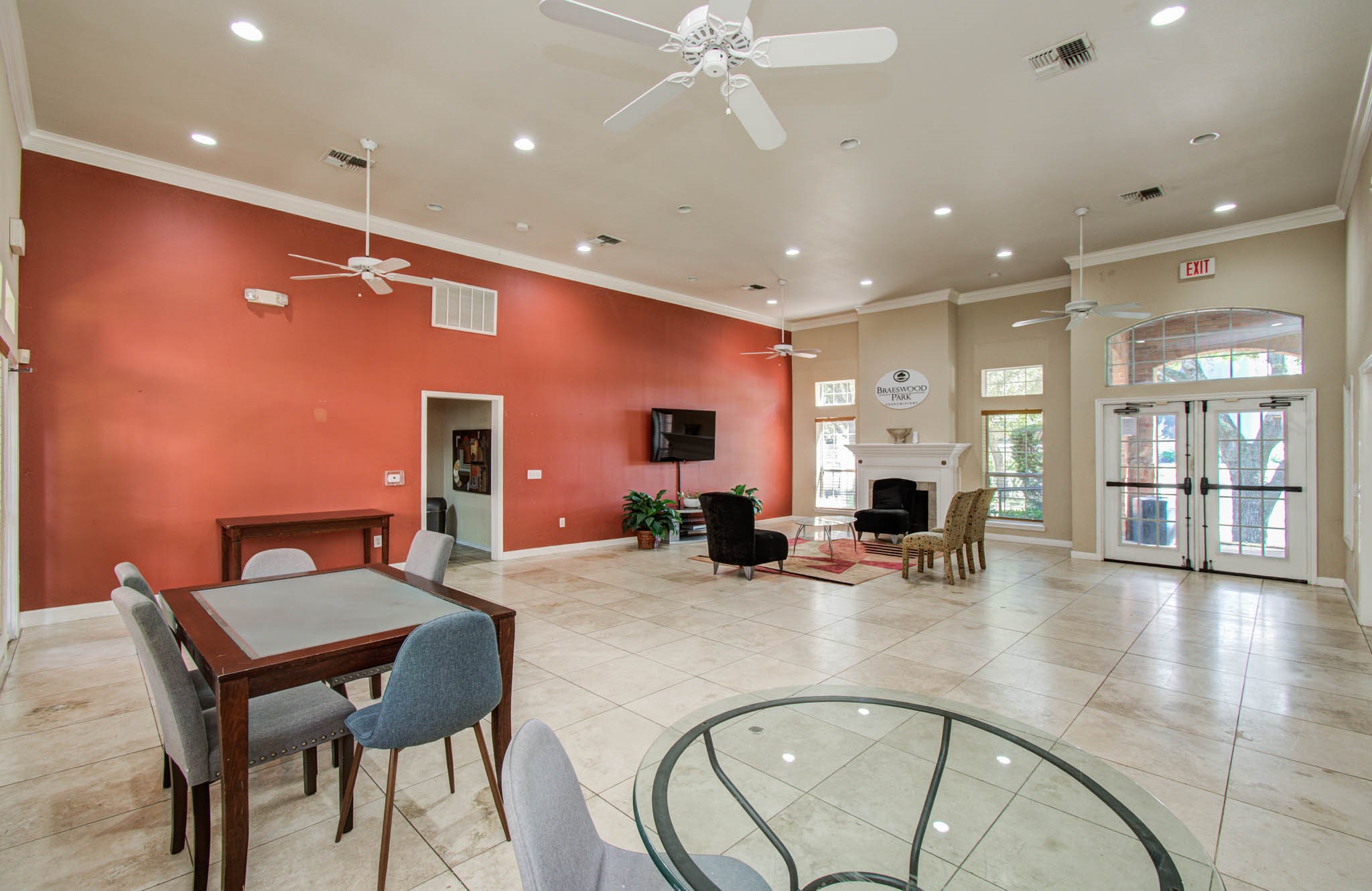 Spacious, well-lit communal area with high ceilings, featuring a cozy seating area by the fireplace, large windows, ceiling fans, and a mix of modern and classic furnishings. Ideal for gatherings or relaxation.