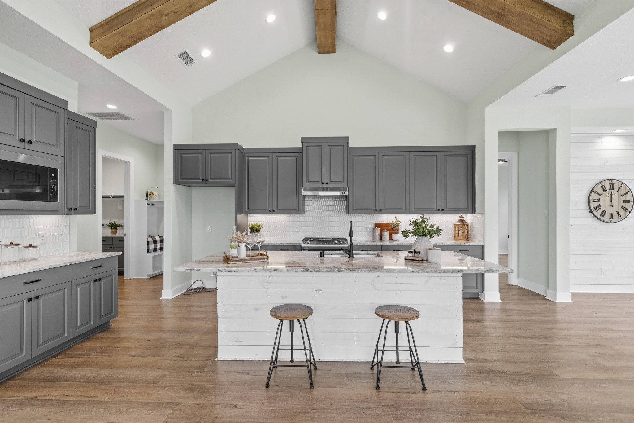 The durable, yet easy maintenance floors flow into this remarkable Kitchen. Below the exposed beamed cathedral ceiling form and function unite.  First, noticed is the abundance of cabinet space along with granite countertops, black hardware, designer backsplash and finished with under cabinet lighting.
