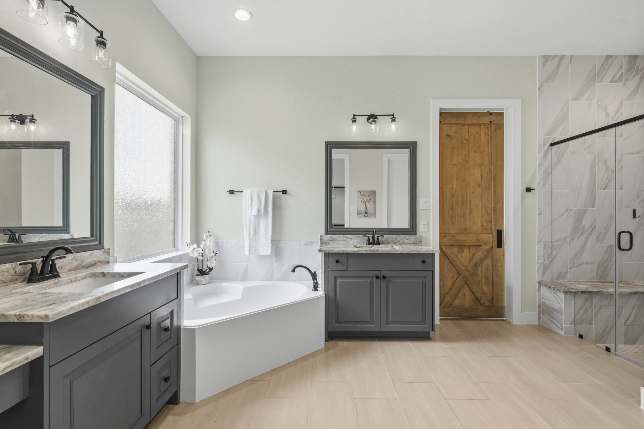 A corner garden tub serves as one focal point and is set beneath a large translucent window that fills the space with natural light while maintaining privacy. The oversized frameless, clear glass shower features a floor-to-ceiling marble-inspired tile and a lovely granite-topped bench seat. Completing this exceptional Bath are two oversized walk-in closets, providing abundant closet space.