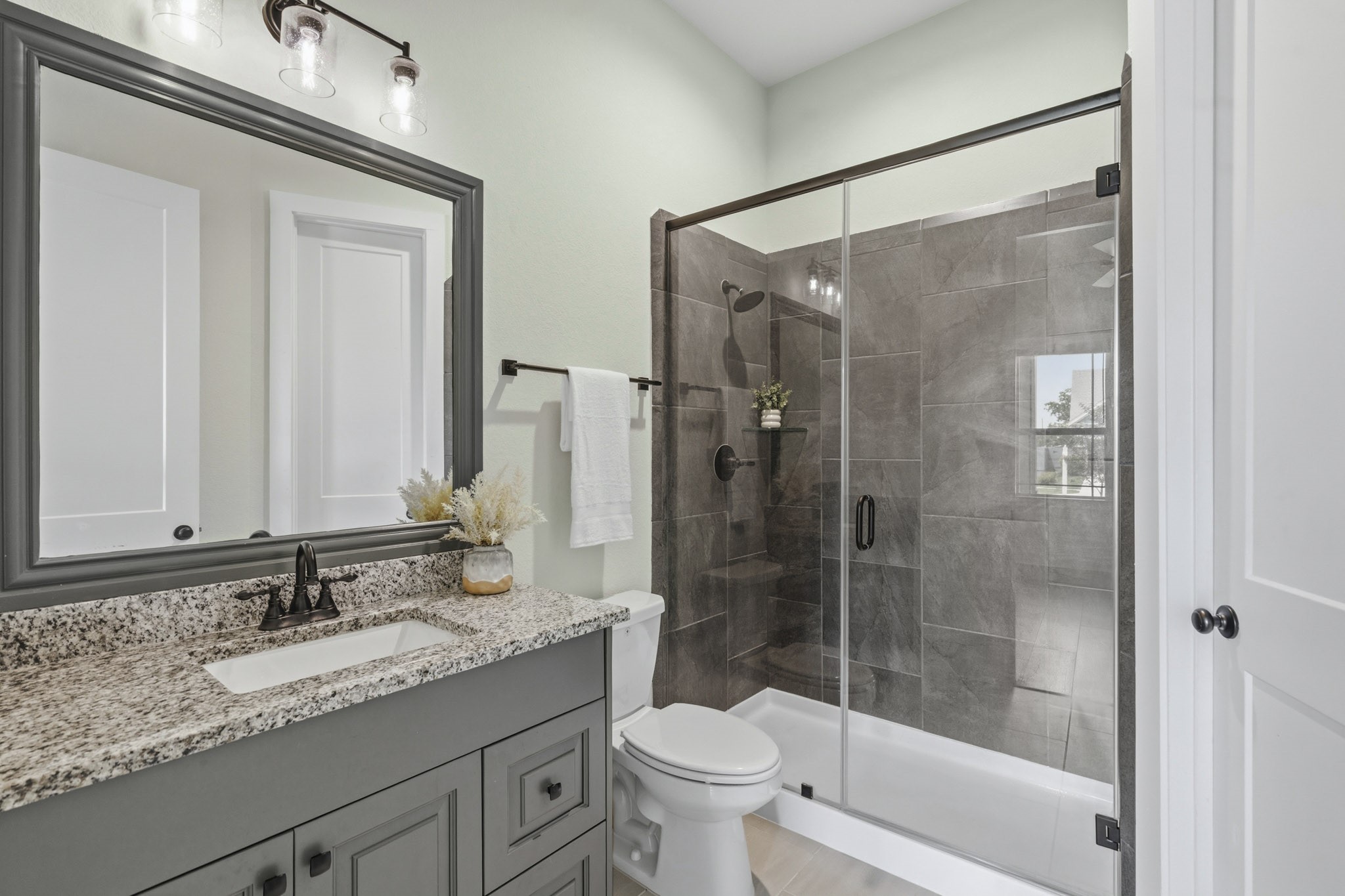 This Guest Bath combines timeless elegance with everyday functionality. The clear glass tub/shower serves as a striking focal point, finish in rich, dark tile that creates a more sophisticated ambiance and adds a sense of luxury to the room. It too, features an undermount sink, sleek granite countertops and a framed mirror.