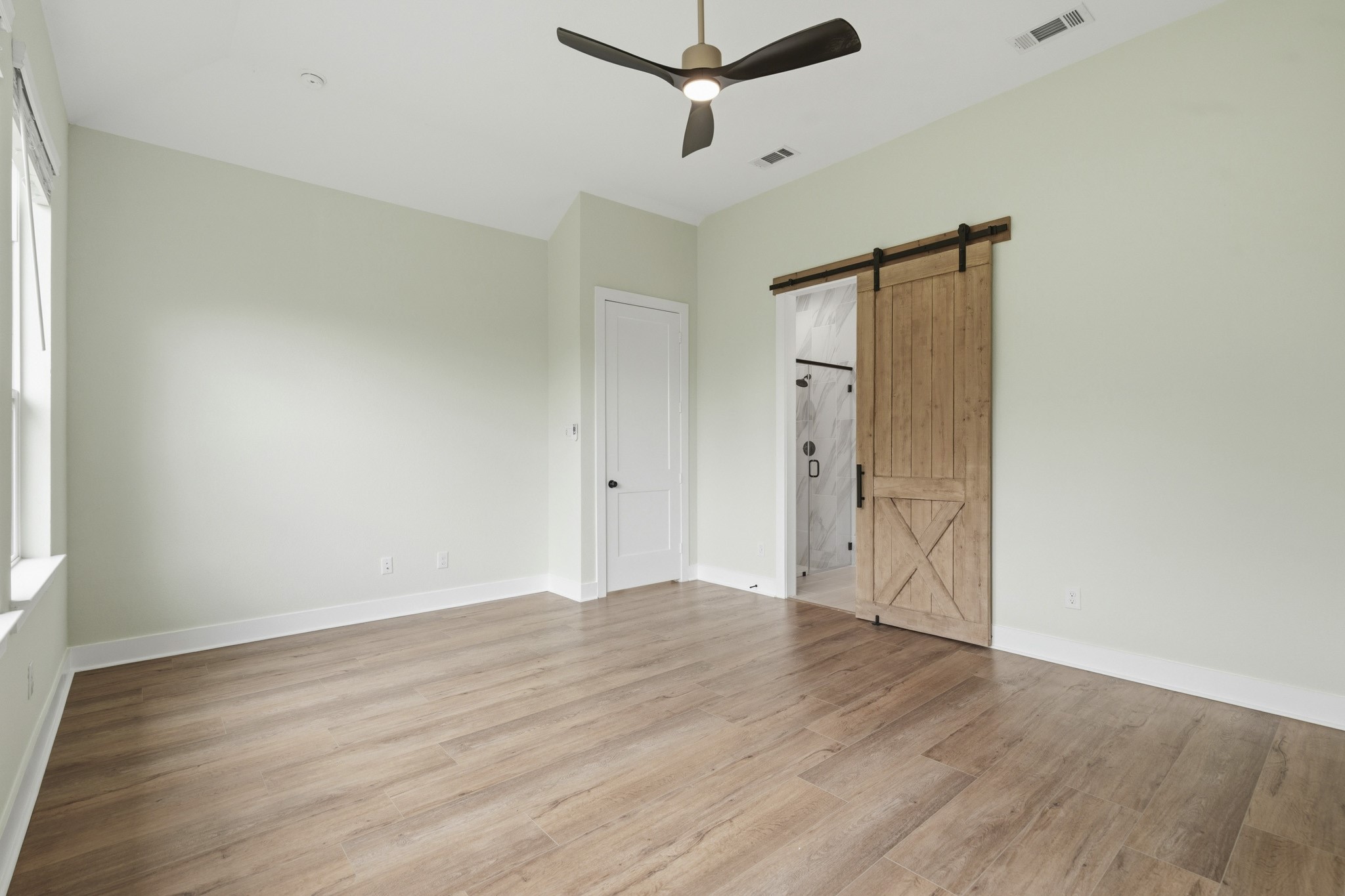 The Primary Bedroom offers exceptional space and versatility, easily accommodating a king-sized bed, matching nightstands, a dresser, and a dedicated media area. A tranquil Retreat with ample room to create your ideal sanctuary. Its finished with a designer black and champagne gold ceiling fan and a custom barn door offering seamless access to the luxurious Bath
