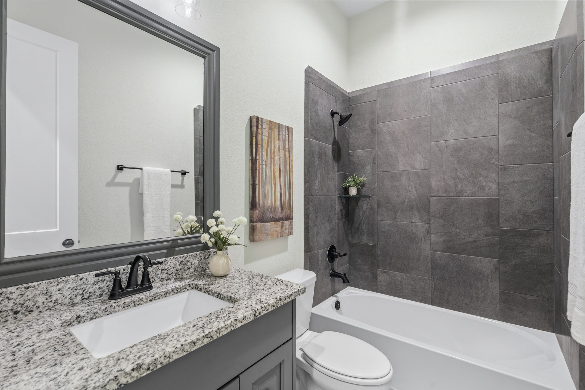 This is a view of the full Bath that serves two Secondary Bedrooms. It is beautifully appointed, featuring a vanity with an undermount sink, granite countertops, and a customed framed mirror that adds another stylish touch. The shower/tub combination also offers a designer's touch to complete the room.