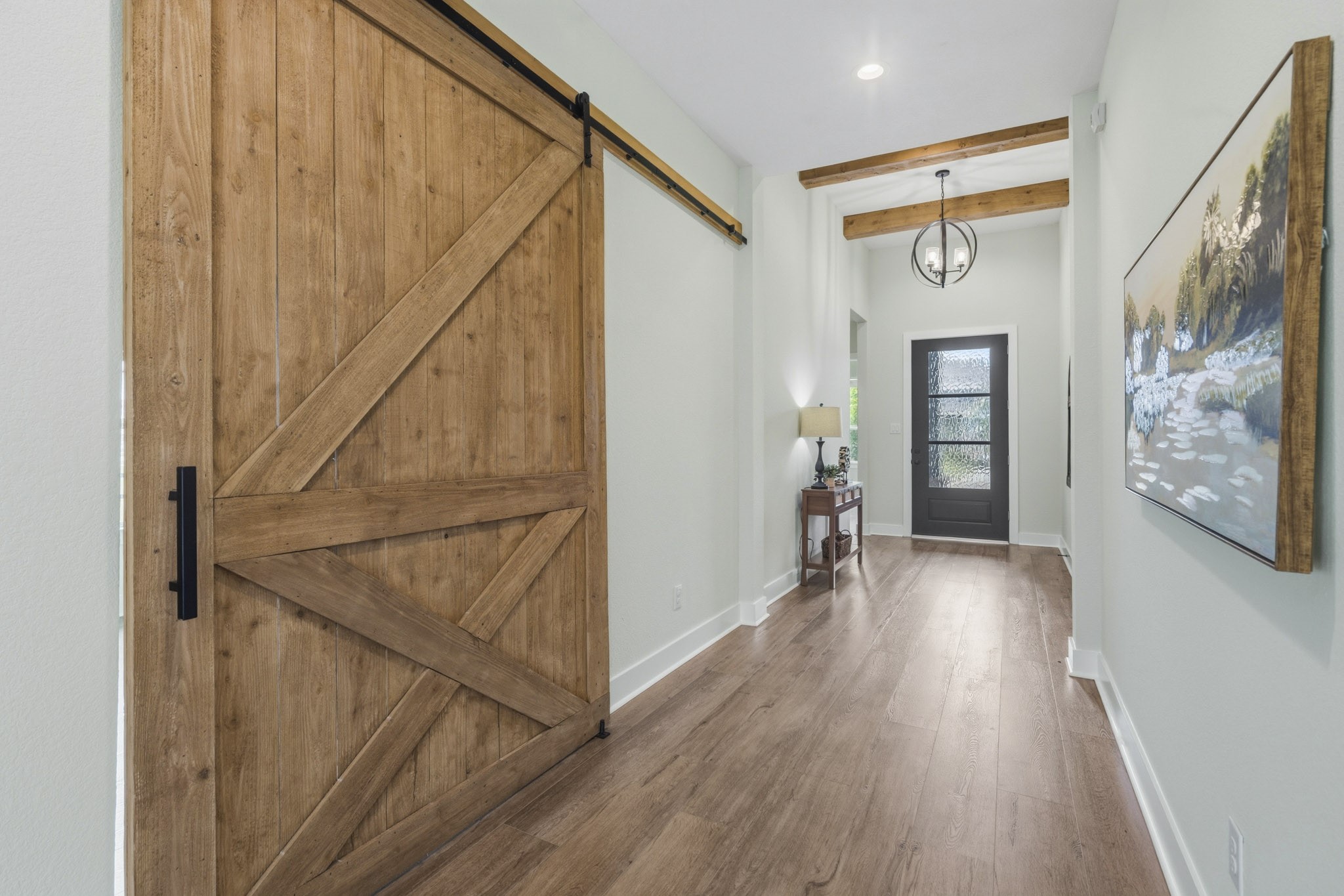 This view of the Foyer captures the striking custom barn door that slides open to the Study and adds warmth and character to the space. An elegant upgraded wrought iron round pendant light illuminates the space. There is also plenty of room for a sofa table or bench seat.