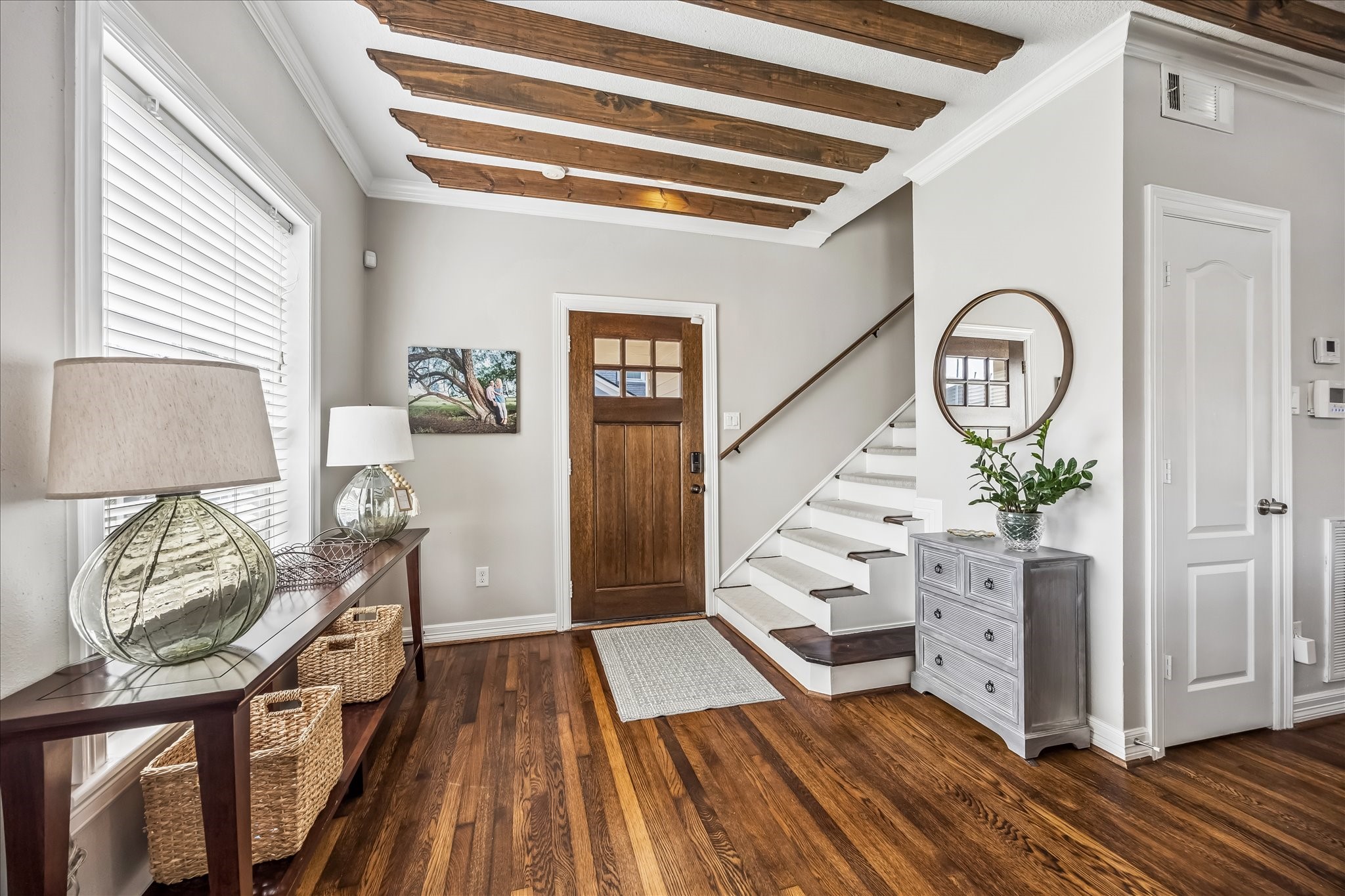 Custom front doors installed in 2020 open to warm wood floors and a staircase finished with custom treads in 2023.