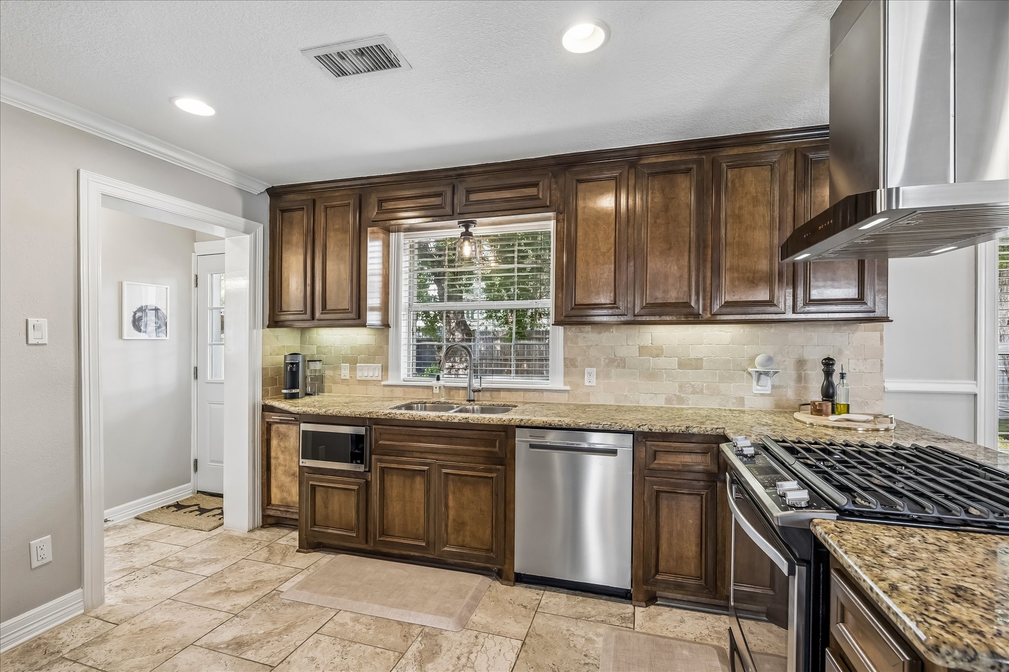 Another angle shows the kitchens generous cabinet run, granite work surfaces, dishwasher, and sink positioned beneath the window.