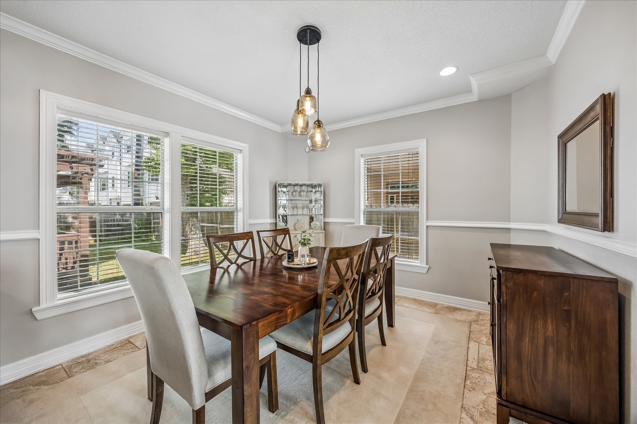 Dining area sits between large windows with chair-rail detailing, warm wood furniture, and a statement pendant overhead.