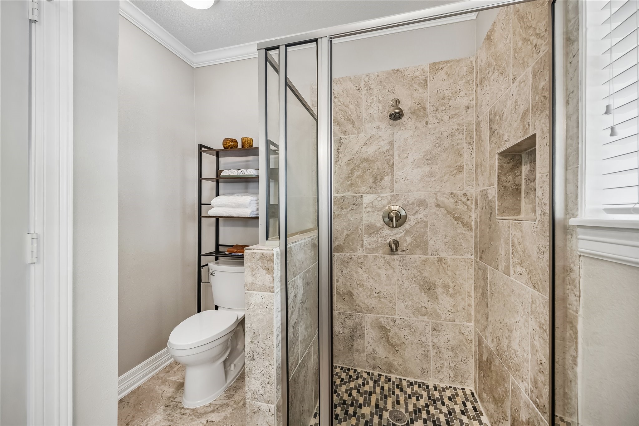 Stone tile wraps the shower from floor to ceiling, complemented by a built-in niche and pebble-style floor detailing.